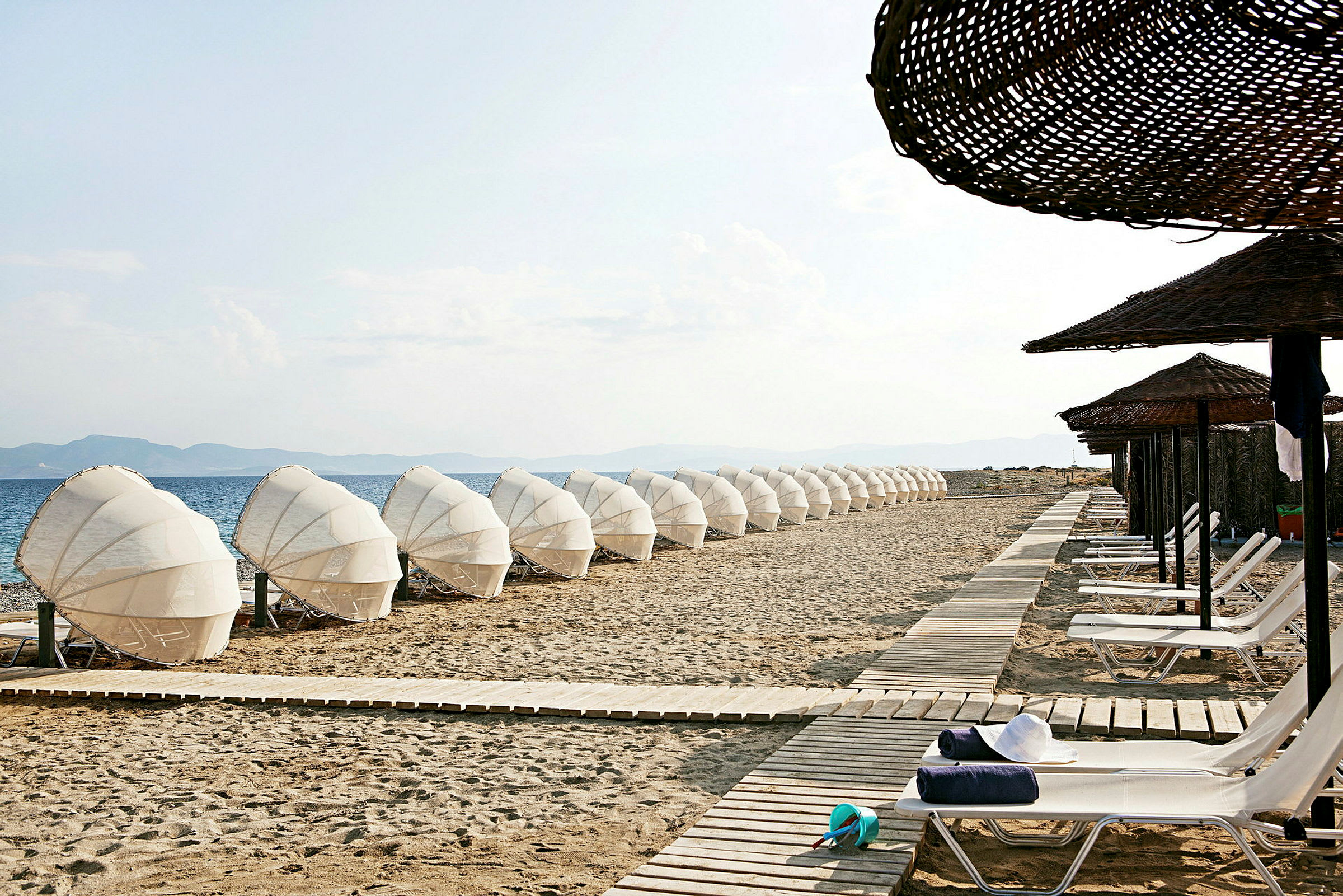 En strand med solsenger og parasoller langs en gangsti. (AI-generert tekst)