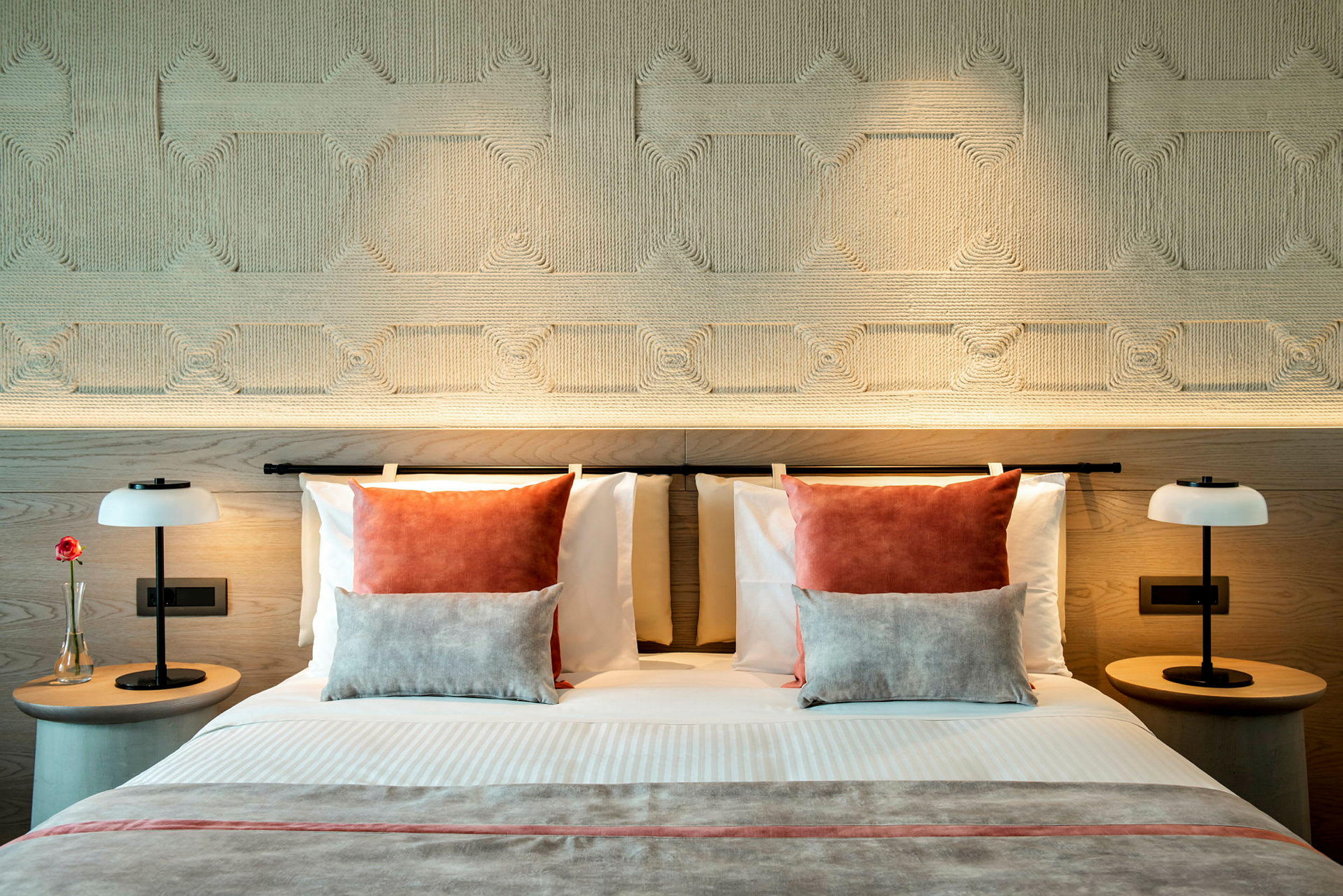 En moderne hotellseng med dekorative puter og symmetriske nattbord utstyrt med lamper. (AI-generert tekst)