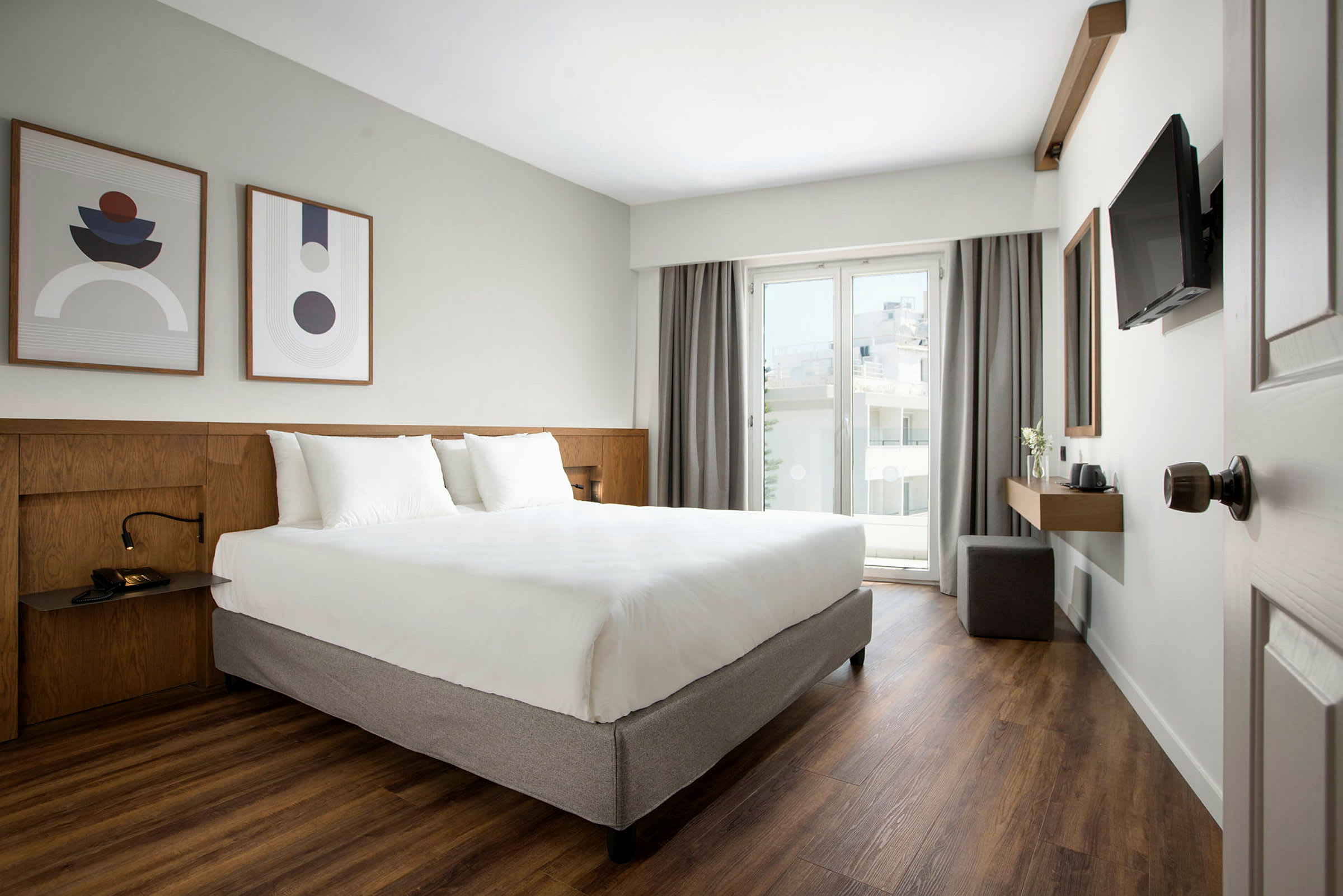Moderne hotellrom med dobbeltseng, kunst på veggen og balkong med glassdør. (AI-generert tekst)