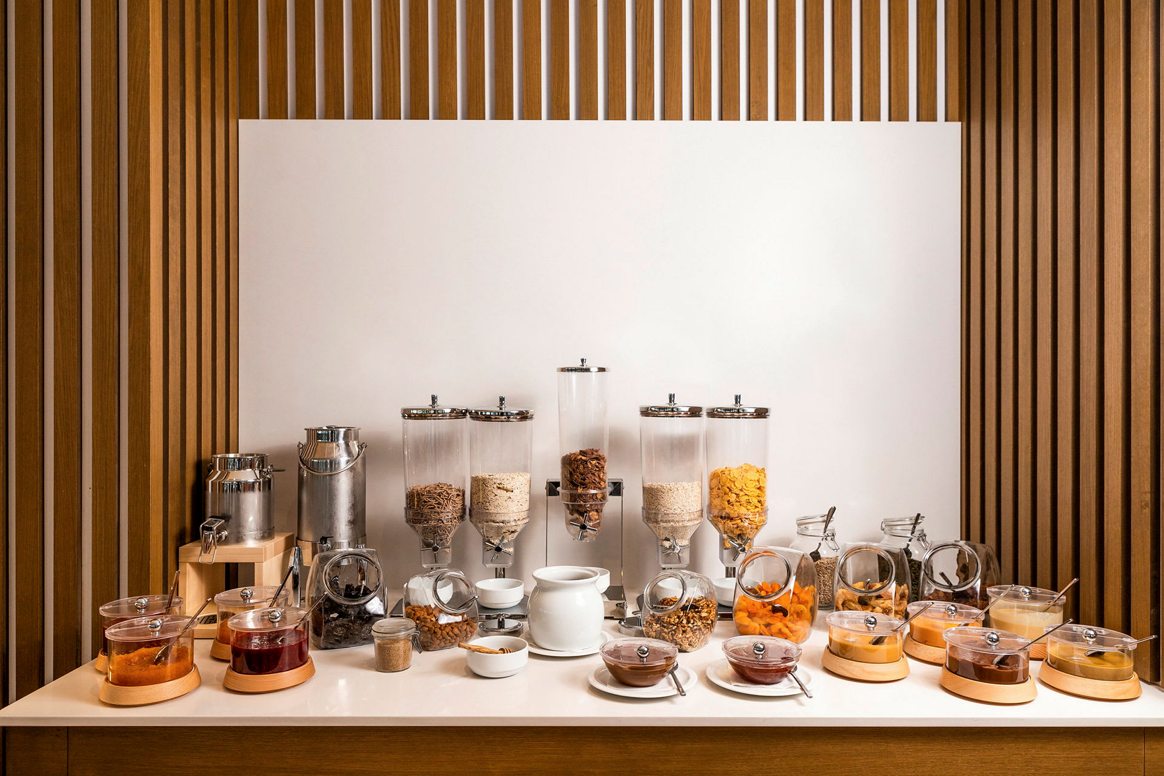 En frokostbuffé med ulike frokostblandinger, tørket frukt, syltetøy og en væskedispenser. (AI-generert tekst)