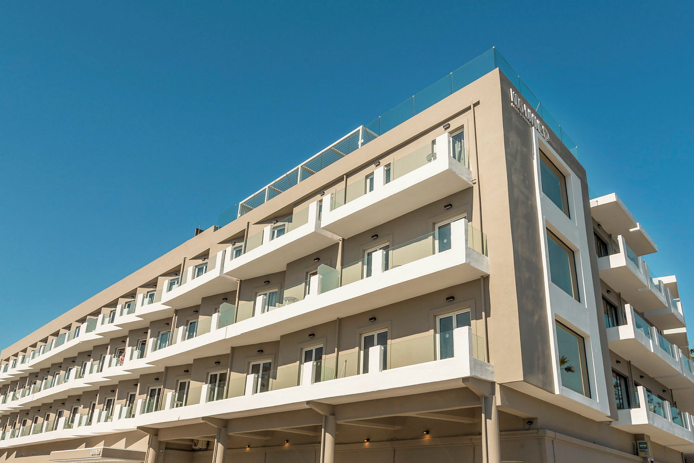 Moderne hotellbygning med flere etasjer og balkonger under en blå himmel. (AI-generert tekst)