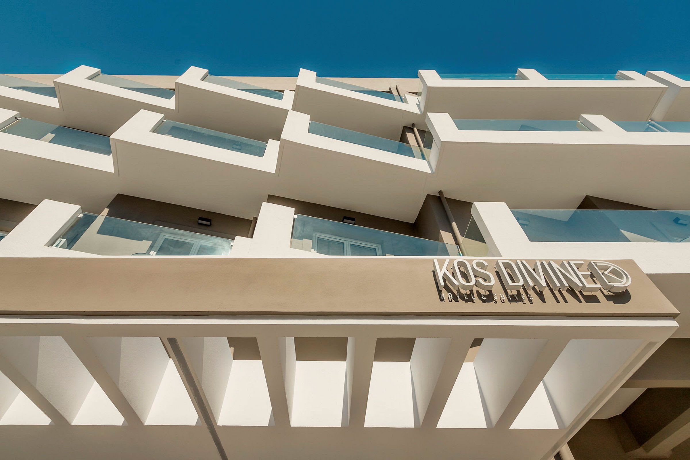 Fasade av en hotellbygning med balkonger i moderne stil og blå himmel i bakgrunnen. (AI-generert tekst)
