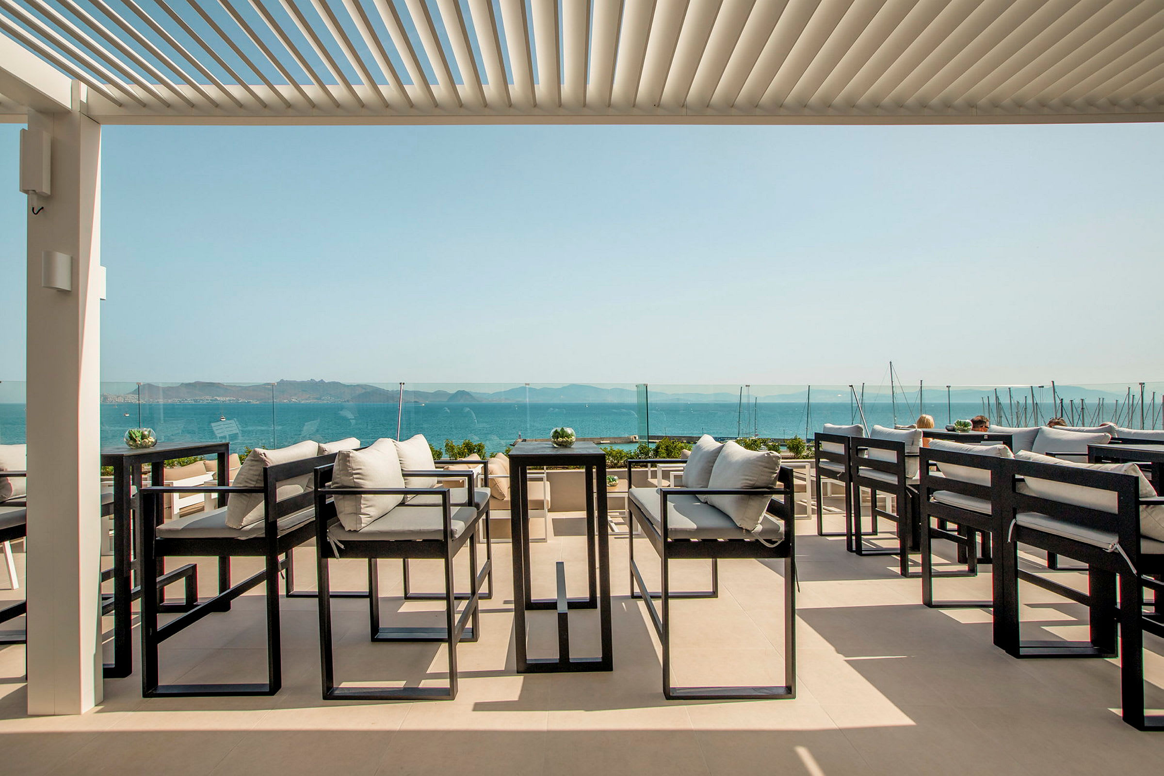En terrasse med moderne sittemøbler, utsikt over havet og en klar, blå himmel. (AI-generert tekst)
