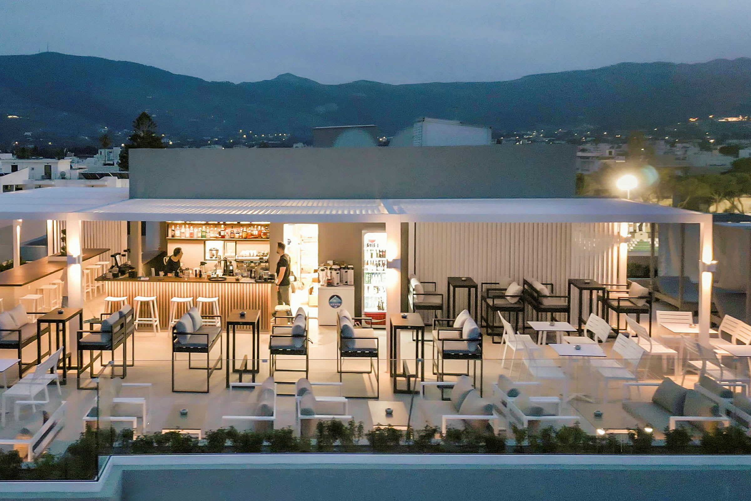 Bilde av en utendørsservering med sitteplasser og en bar på en takterrasse i skumringen. (AI-generert tekst)