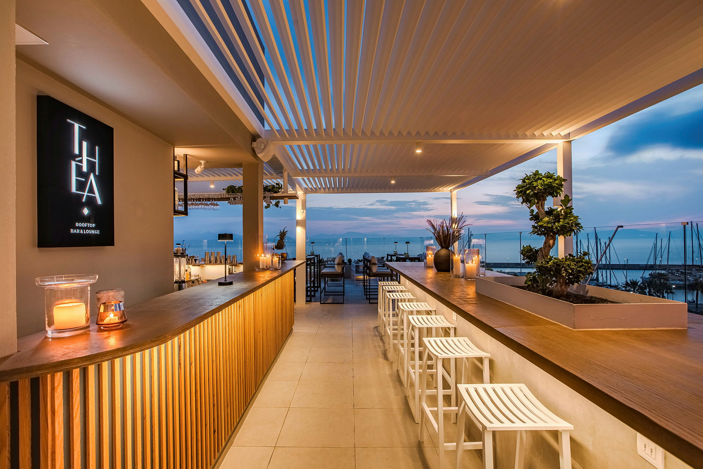 En moderne takterrasse med utsikt over havet i solnedgangen. Baren er opplyst og koselig innredet. (AI-generert tekst)
