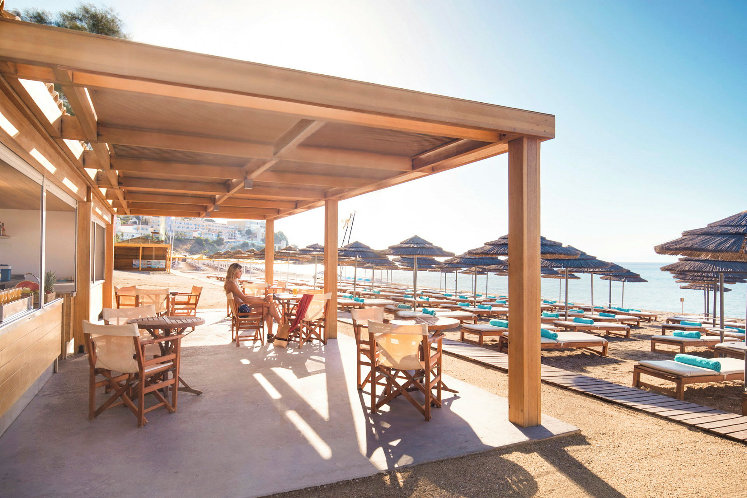 Terrasse med trestoler under solskjerming ved en strand. (AI-generert tekst)
