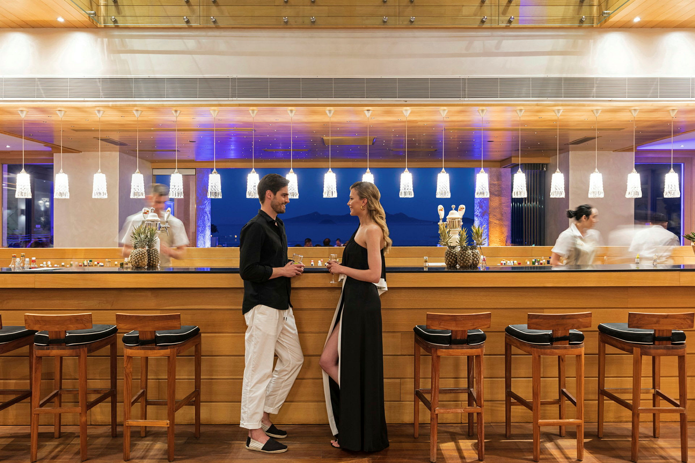 Personer står ved en elegant bar med treinteriør og belysning. (AI-generert tekst)