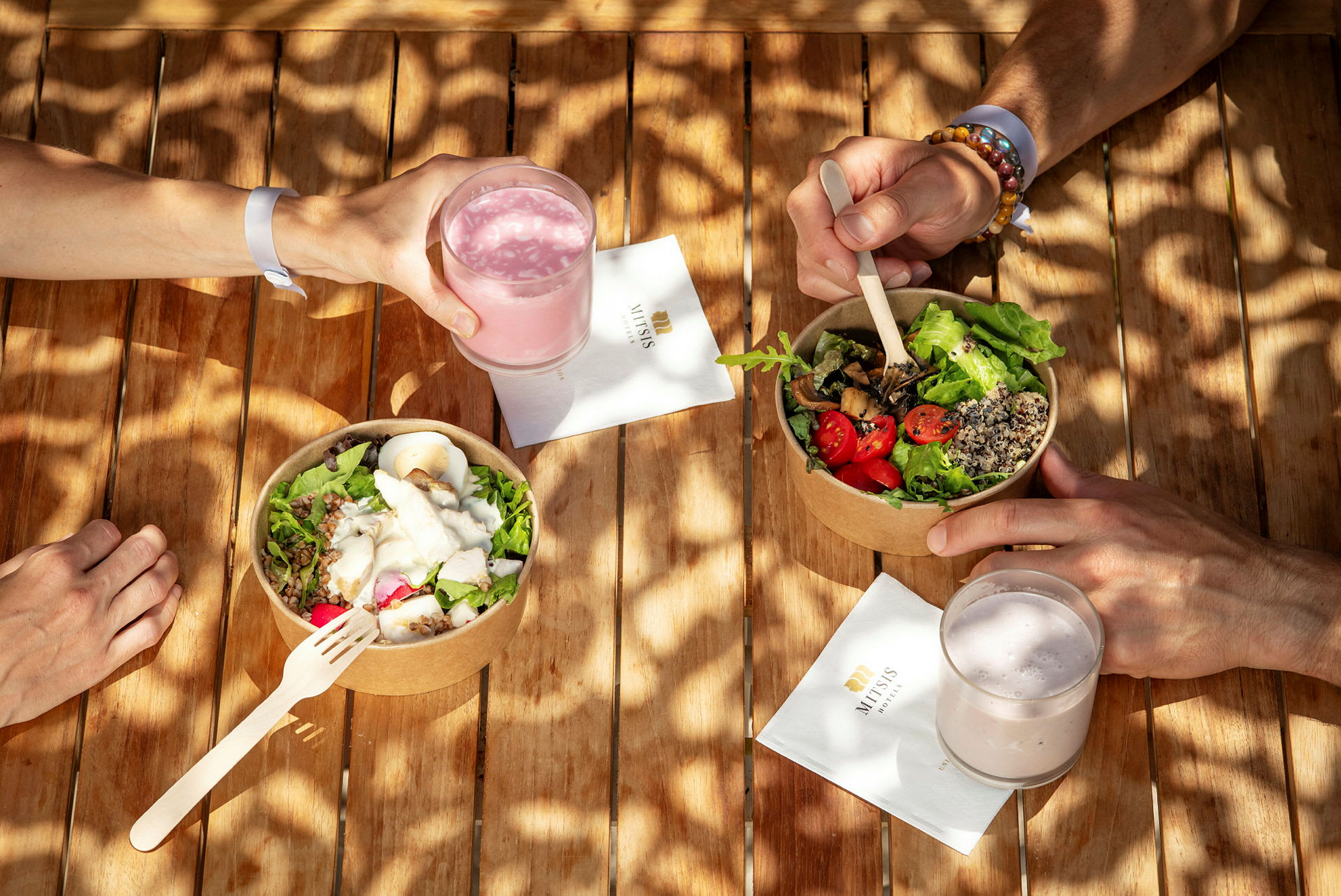 En hånd holder et glass med rosa drikke ved siden av to boller med salat. (AI-generert tekst)