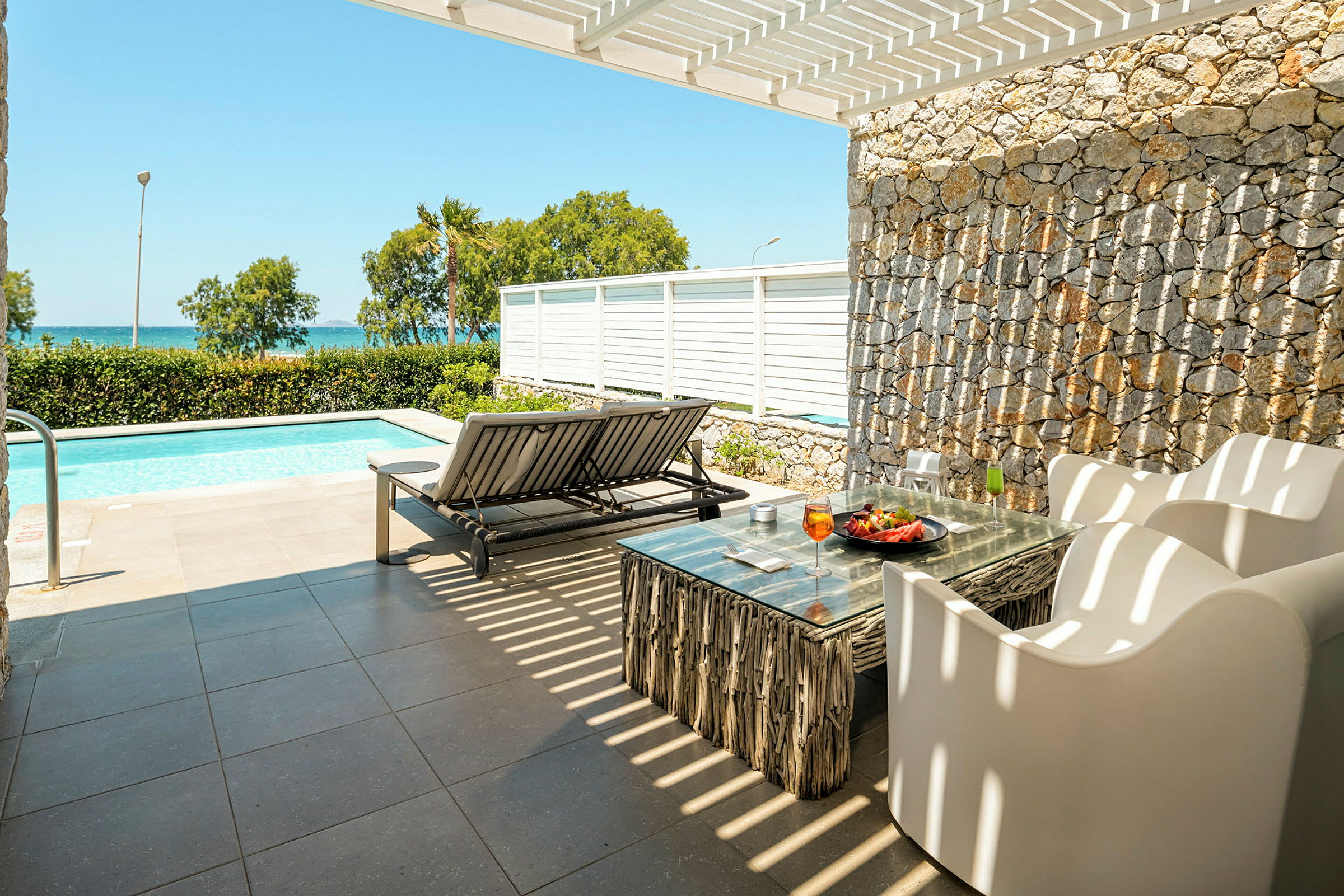 Terrasse med utemøbler og solseng ved et basseng, med havutsikt i bakgrunnen. (AI-generert tekst)