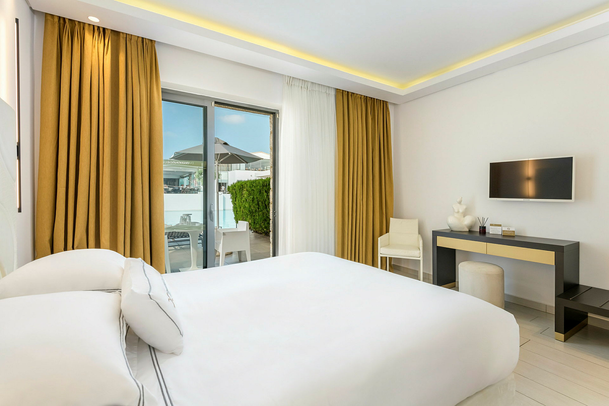 Hotellrom med hvit innredning, en dobbeltseng, skrivebord og utgang til terrasse. (AI-generert tekst)