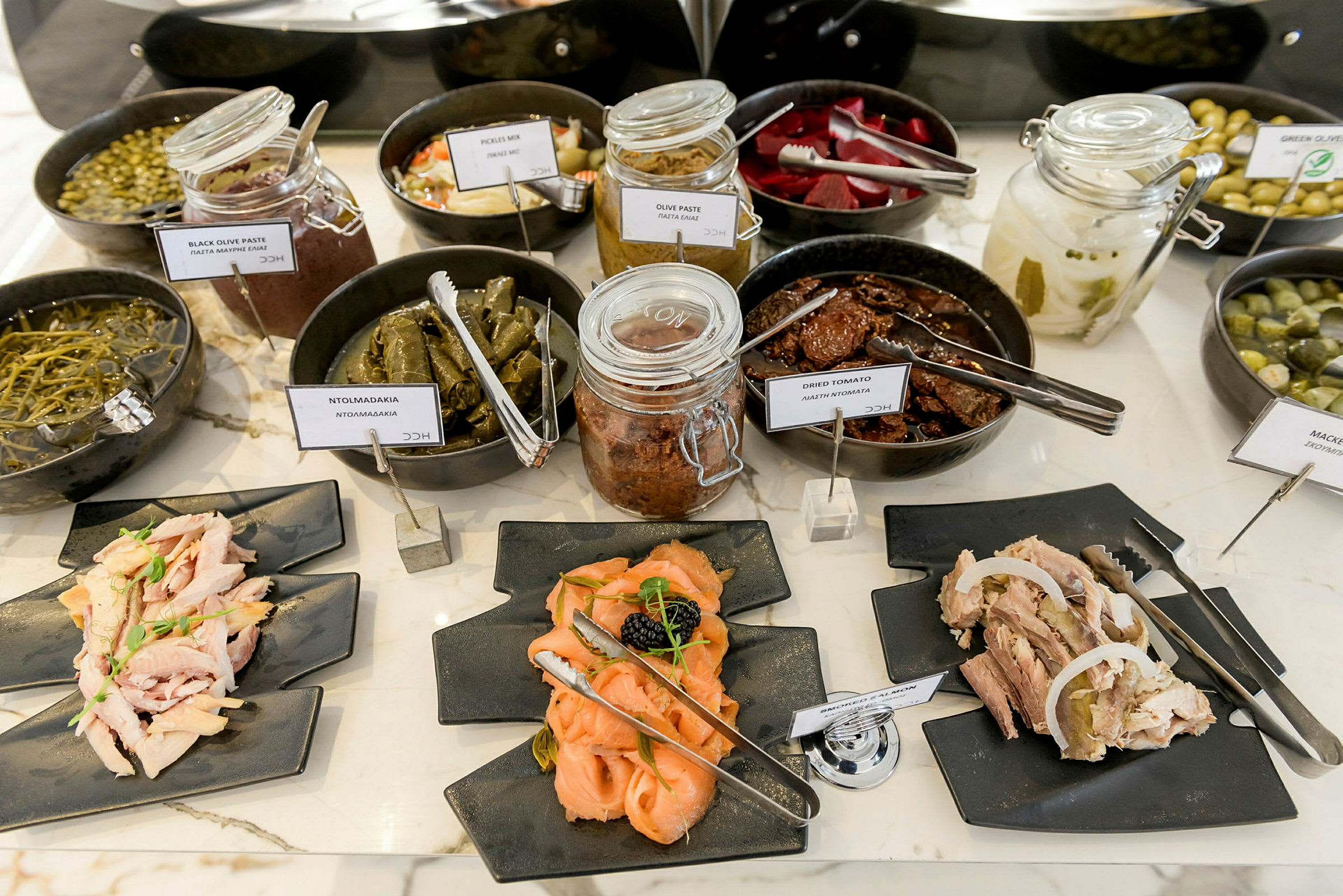 Buffet med ulike typer appetittvekkere og småretter, inkludert syltet mat og kaldskåret på tallerkener. (AI-generert tekst)