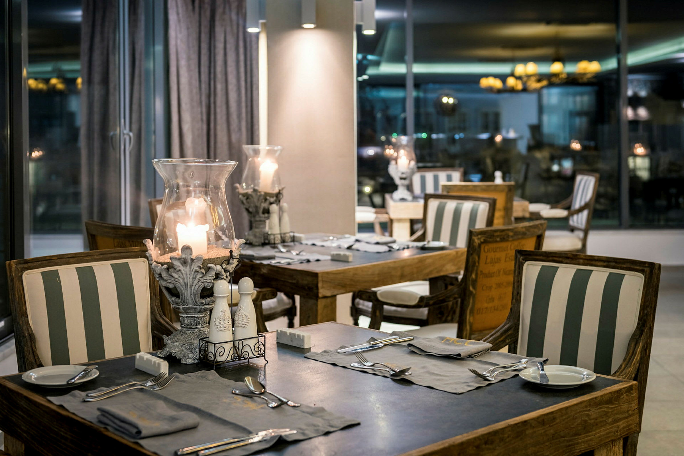 En restaurant med bord og stoler dekorert med stripete puter og tente lys. (AI-generert tekst)