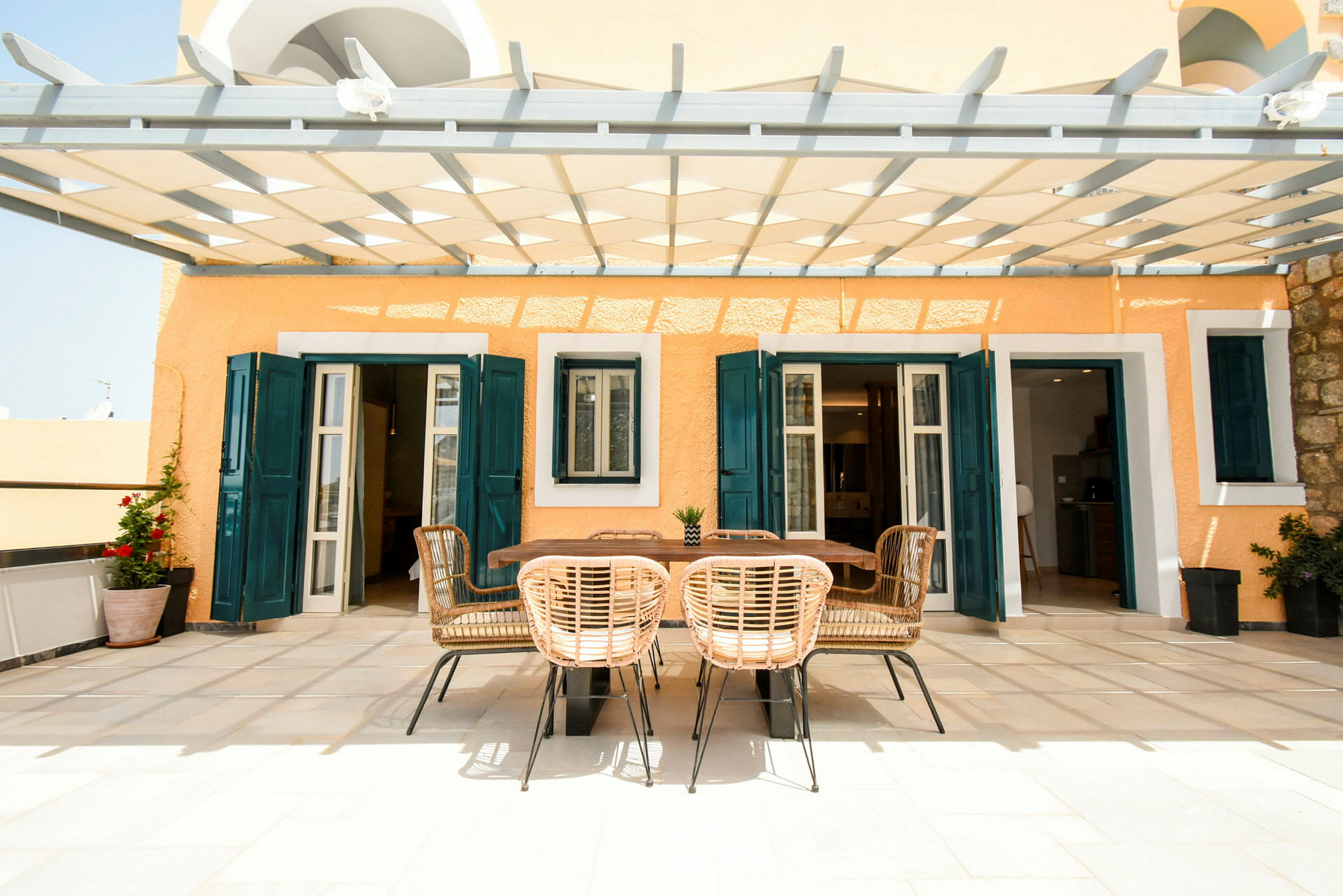 En terrasse med en spiseplass under en pergola, omgitt av fargede husvegger. (AI-generert tekst)