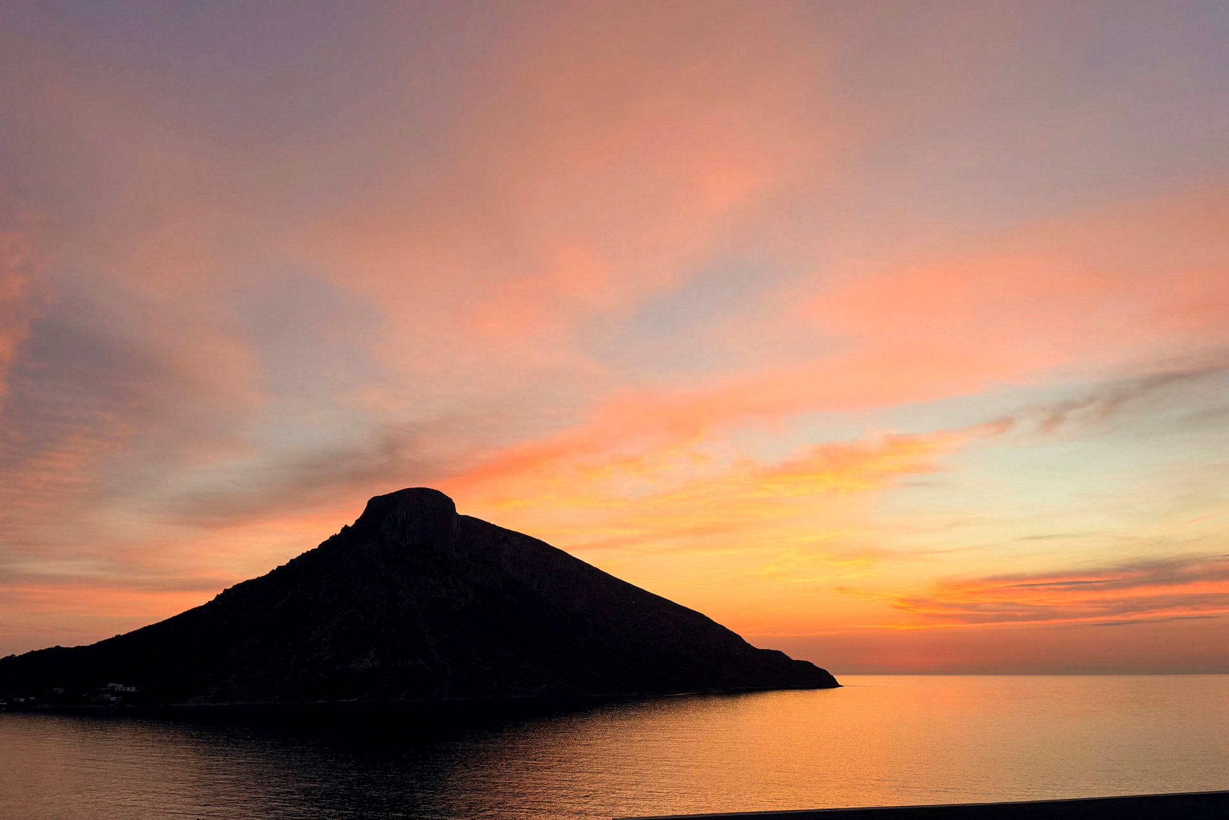 En silhuett av en høyde ved sjøen mot en fargerik solnedgang. (AI-generert tekst)