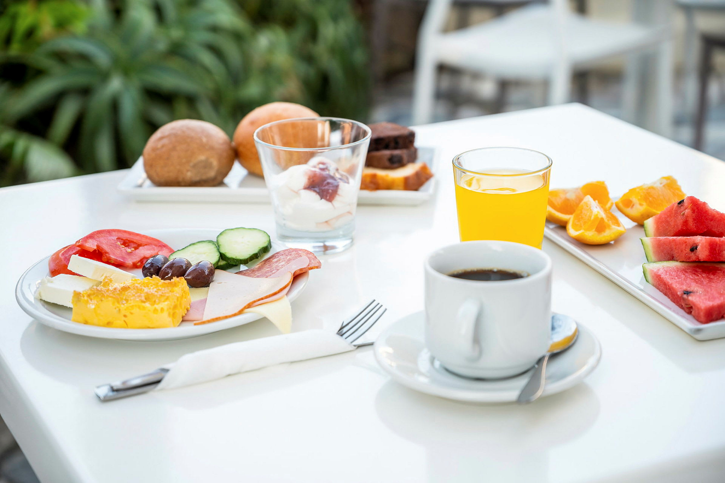 En frokost med kaffe, appelsinjuice, brød, frukt og grønnsaker på et bord. (AI-generert tekst)