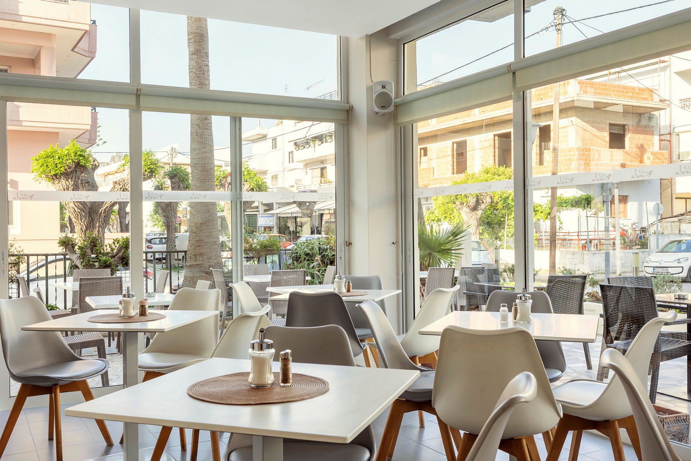 En lys restaurant med vinduer ut mot gaten og utendørsbord. (AI-generert tekst)