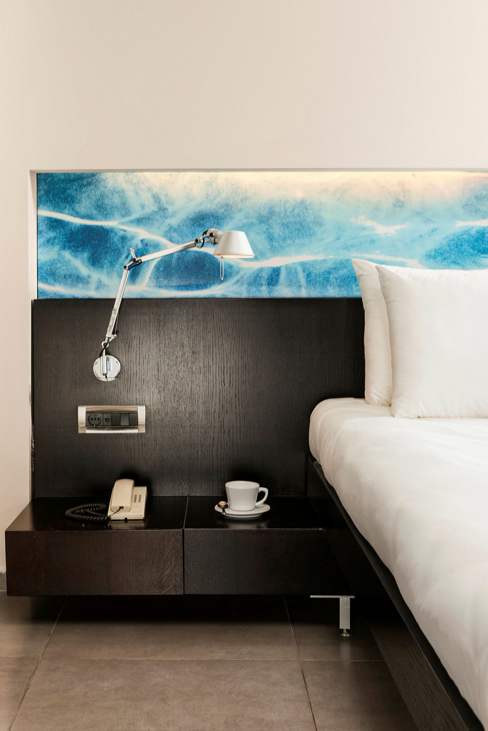 Hotellrom med seng, nattbord, lampe og telefon. (AI-generert tekst)