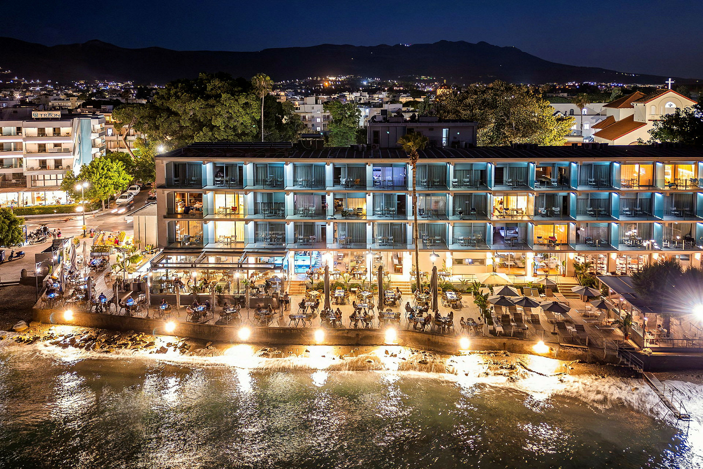 Hotellbygning og restaurant ved vannet, opplyst om kvelden. (AI-generert tekst)