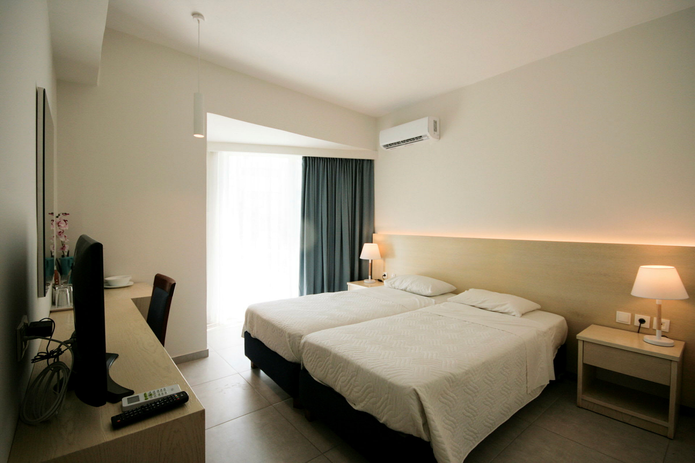 Hotellrom med to enkeltsenger, skrivebord med TV og lampe på nattbordet. (AI-generert tekst)