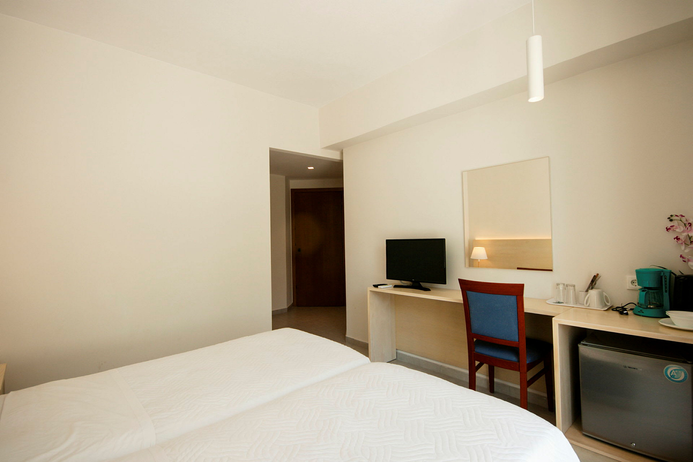 Interiøret i et hotellrom med to enkeltsenger, skrivebord med stol, TV, lite kjøleskap og kaffemaskin. (AI-generert tekst)