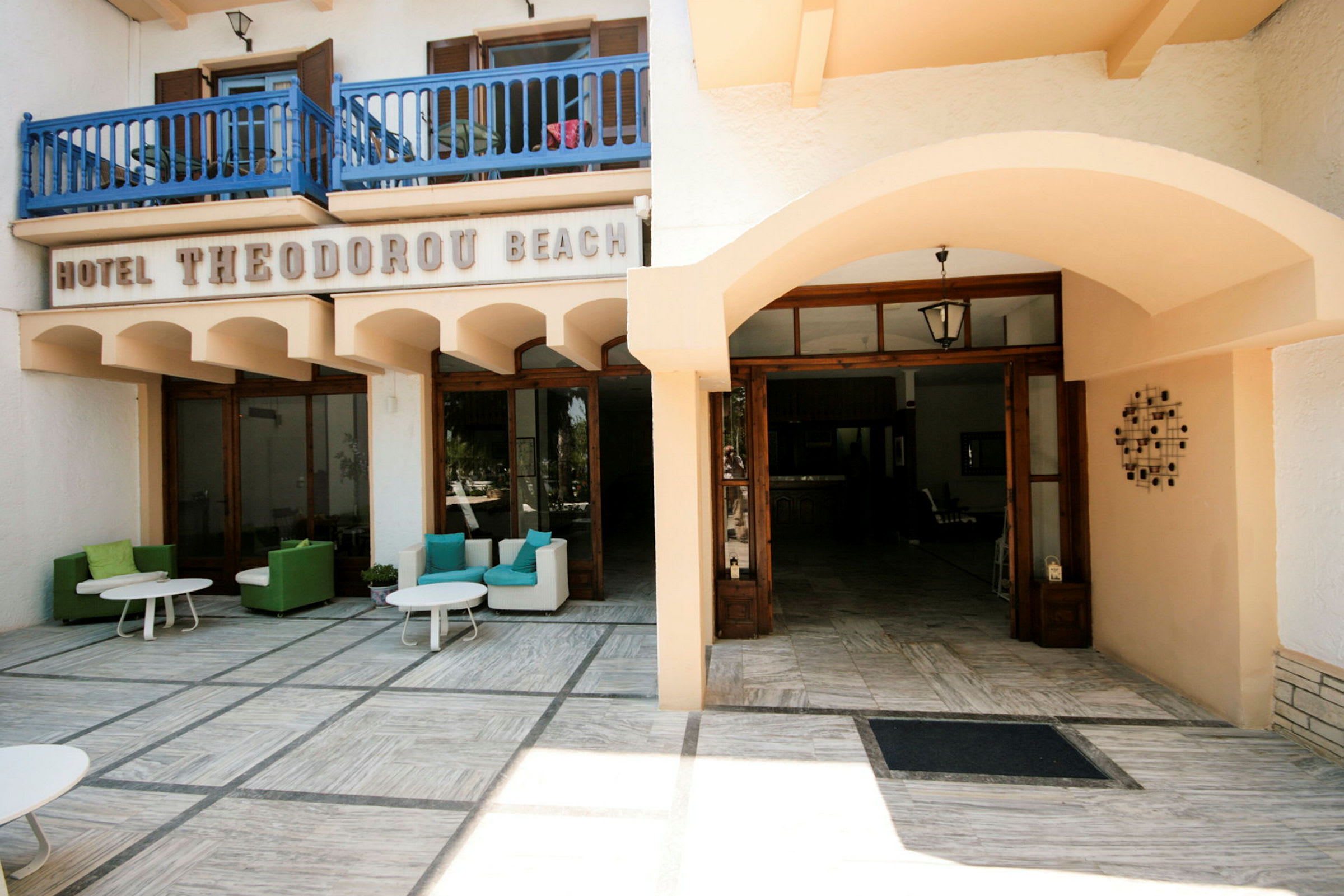 Inngang til Hotel Theodoru Beach med uteområder for sitteplasser. (AI-generert tekst)