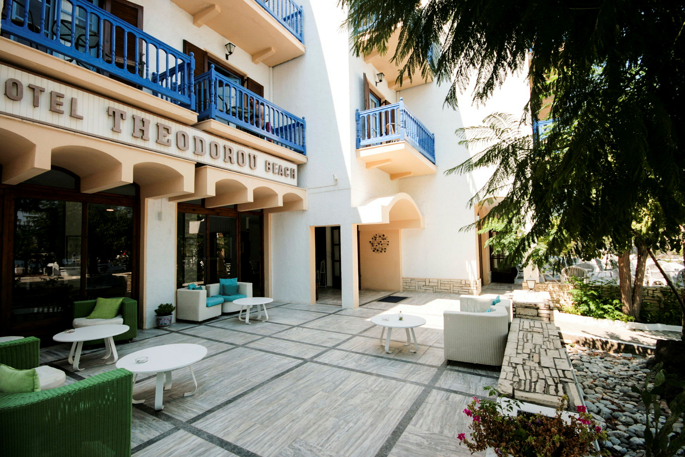 Eksteriør av et hotell med terrasse med sittegrupper under blå balkonger. (AI-generert tekst)