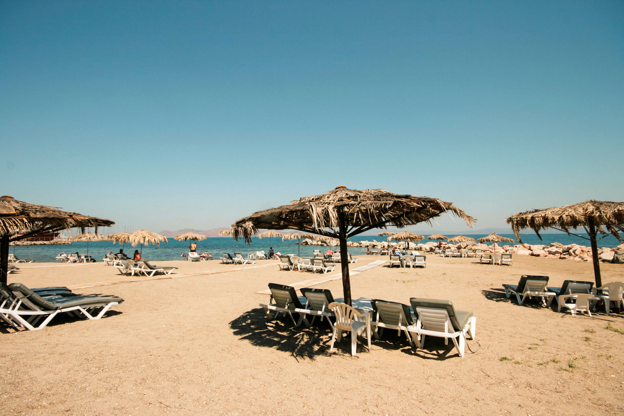 Strand med solsenger og parasoller laget av halmtak. (AI-generert tekst)