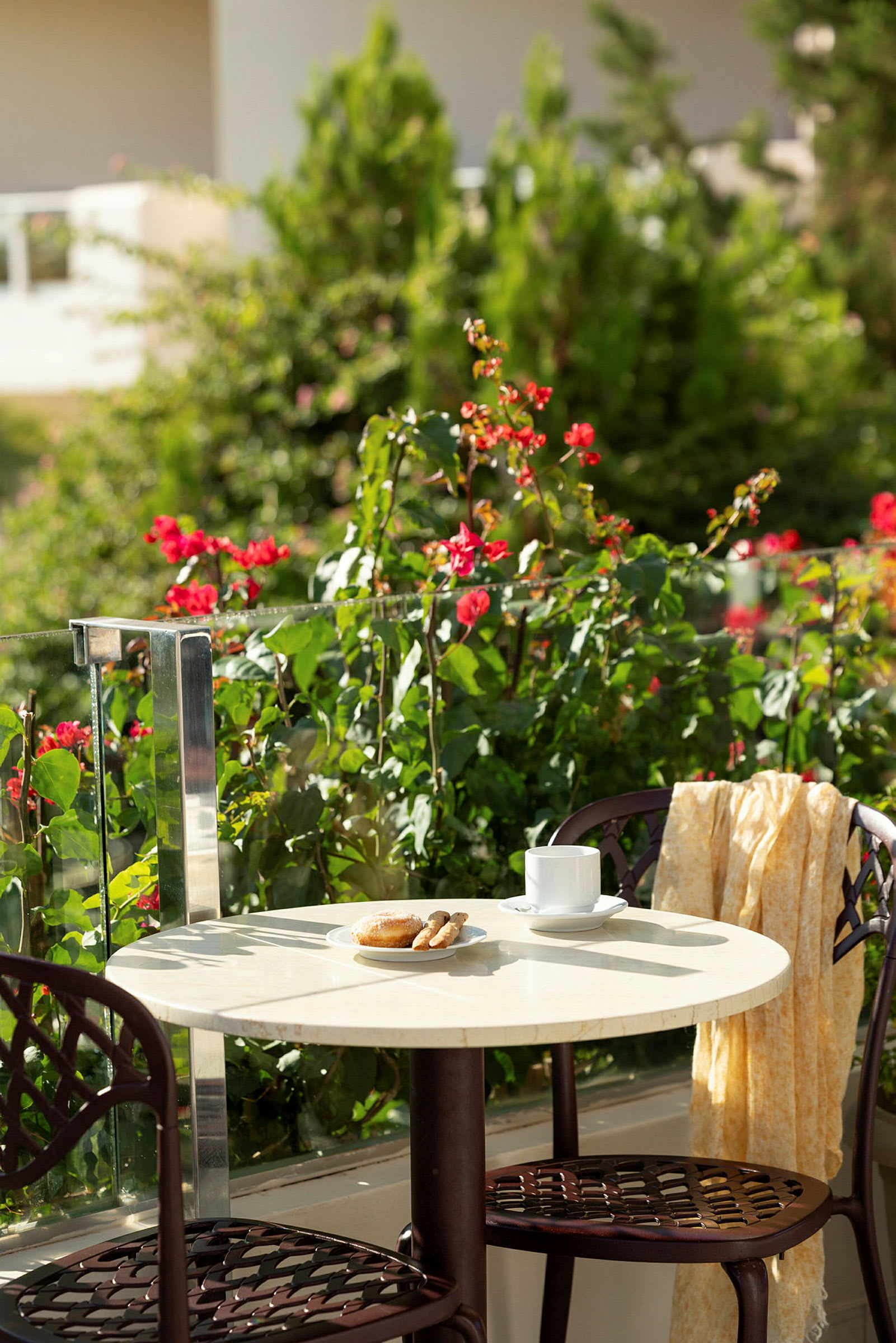 Bord med kaffekopp, bakverk og stoler på terrasse med en frodig omgivelse. (AI-generert tekst)