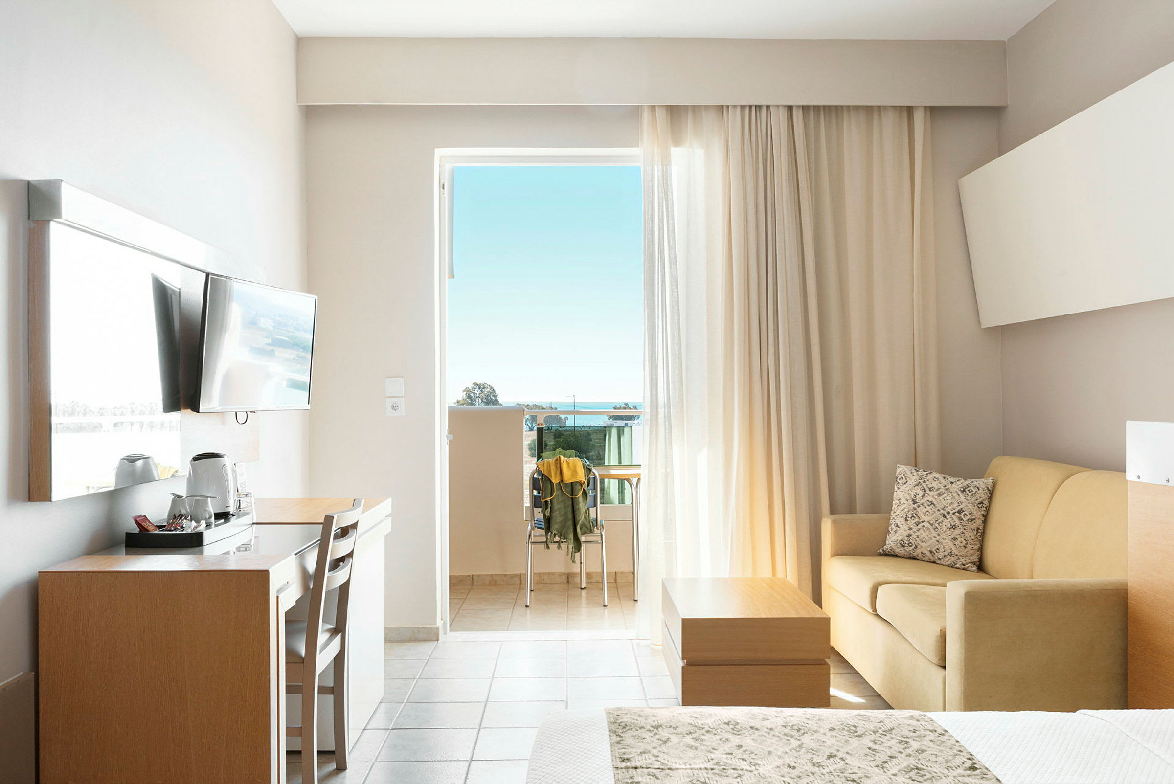 Hotellrom med balkong, TV, skrivebord, sofa og seng. (AI-generert tekst)