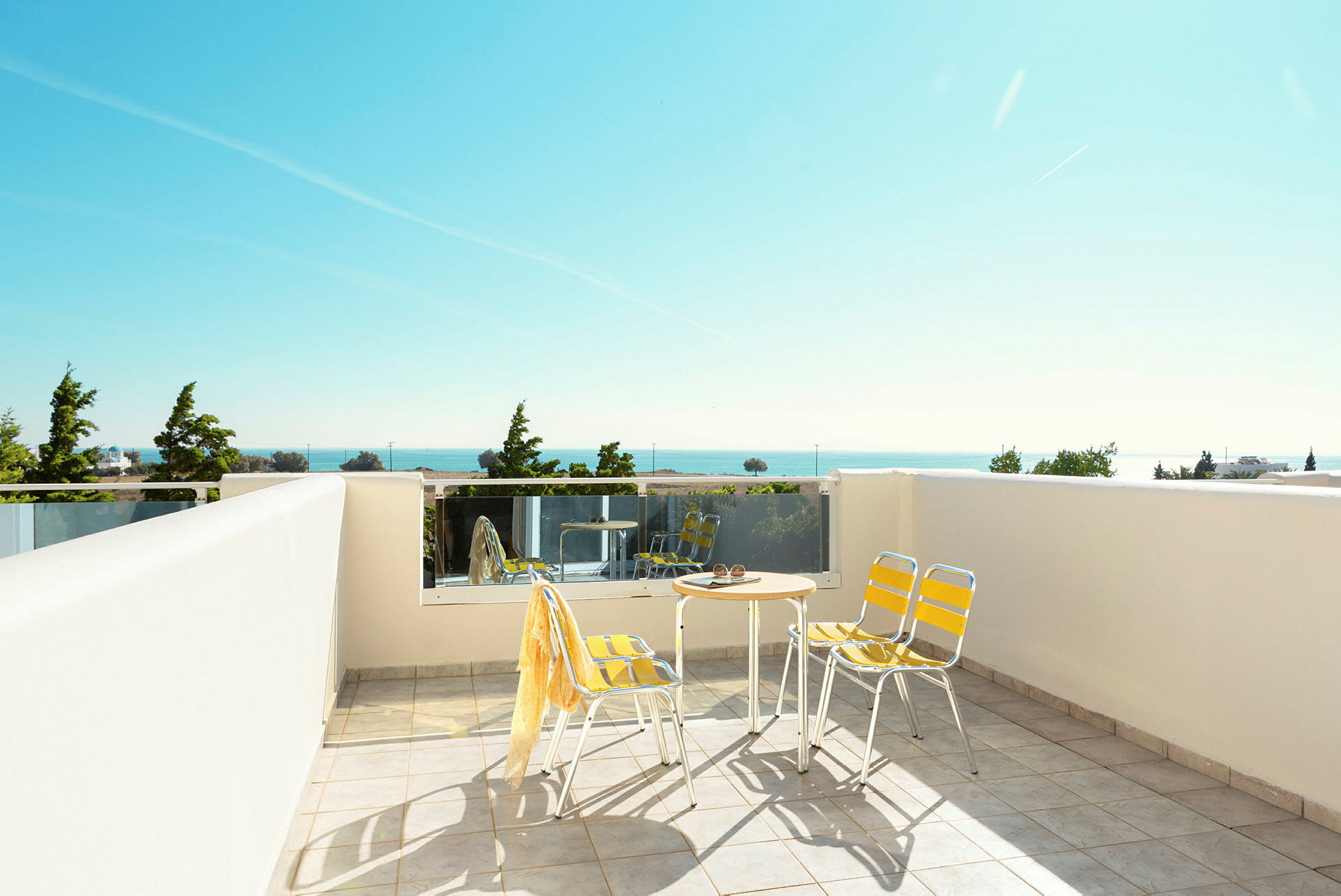 En terrasse med bord og stoler, utsikt mot havet og grøntområder. (AI-generert tekst)