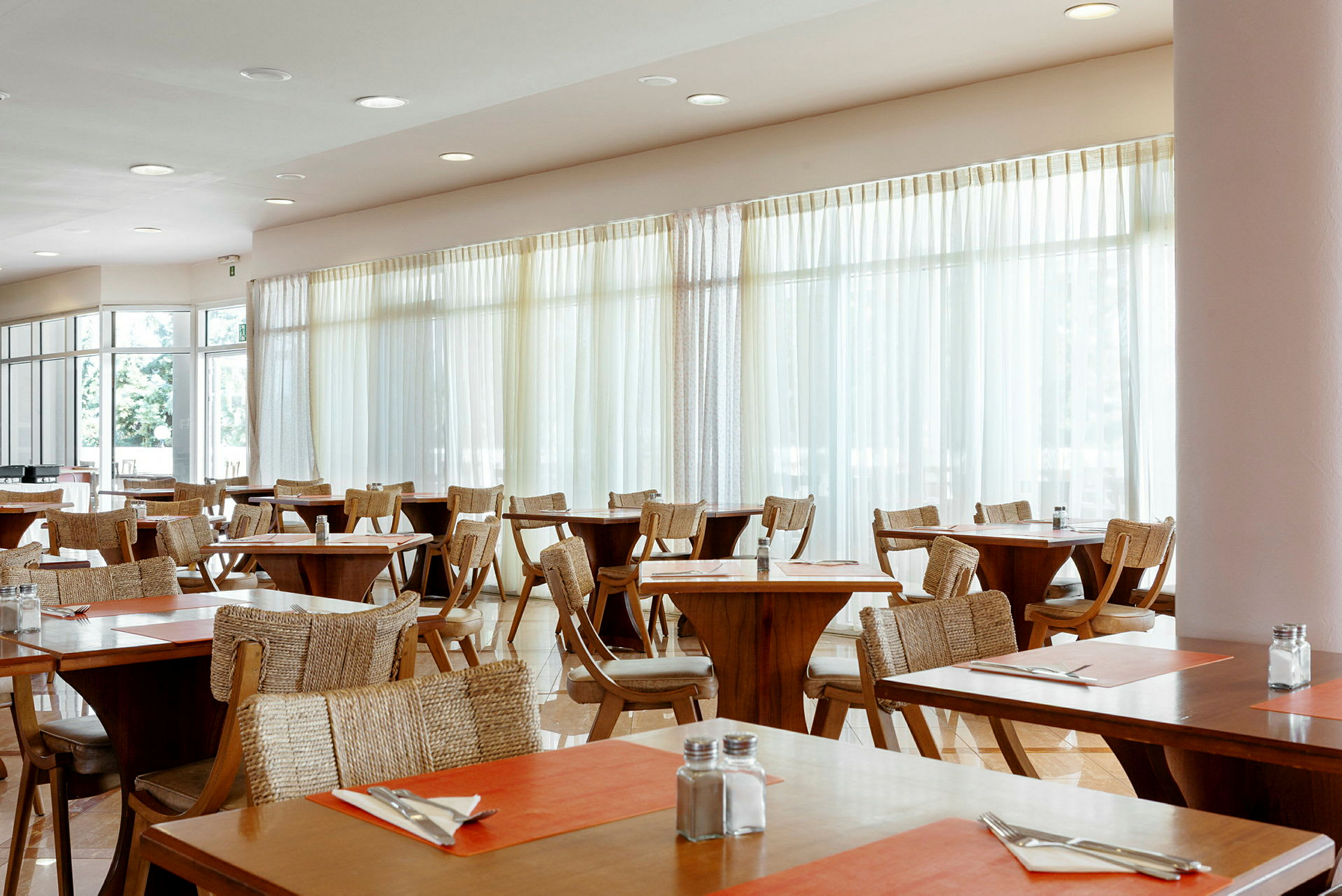 En restaurant med trebord og stoler, dekorert med oransje bordmatter og oppsatt bestikk. (AI-generert tekst)