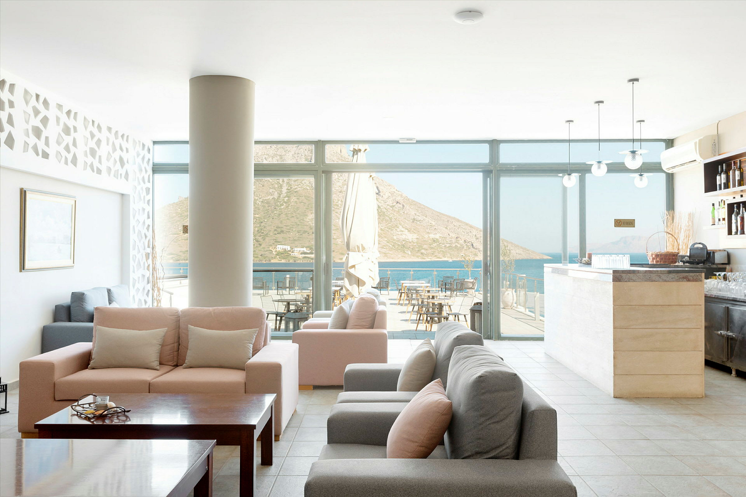 En hotellobby med komfortable sofaer, et bord og glassvegger som viser utsikten mot havet og fjellene. (AI-generert tekst)