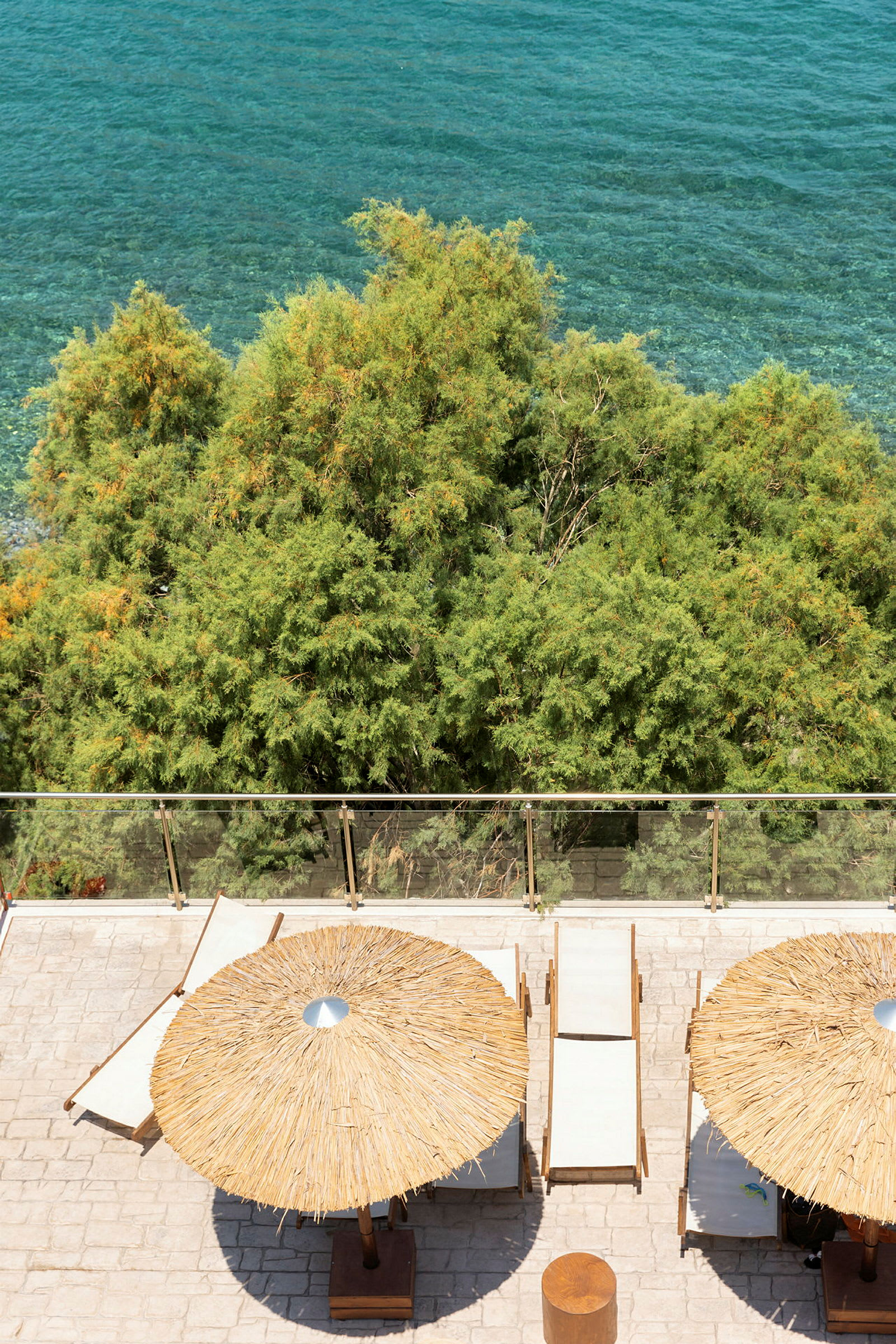 Strandstoler og parasoller på en terrasse med utsikt over havet og grønne trær. (AI-generert tekst)