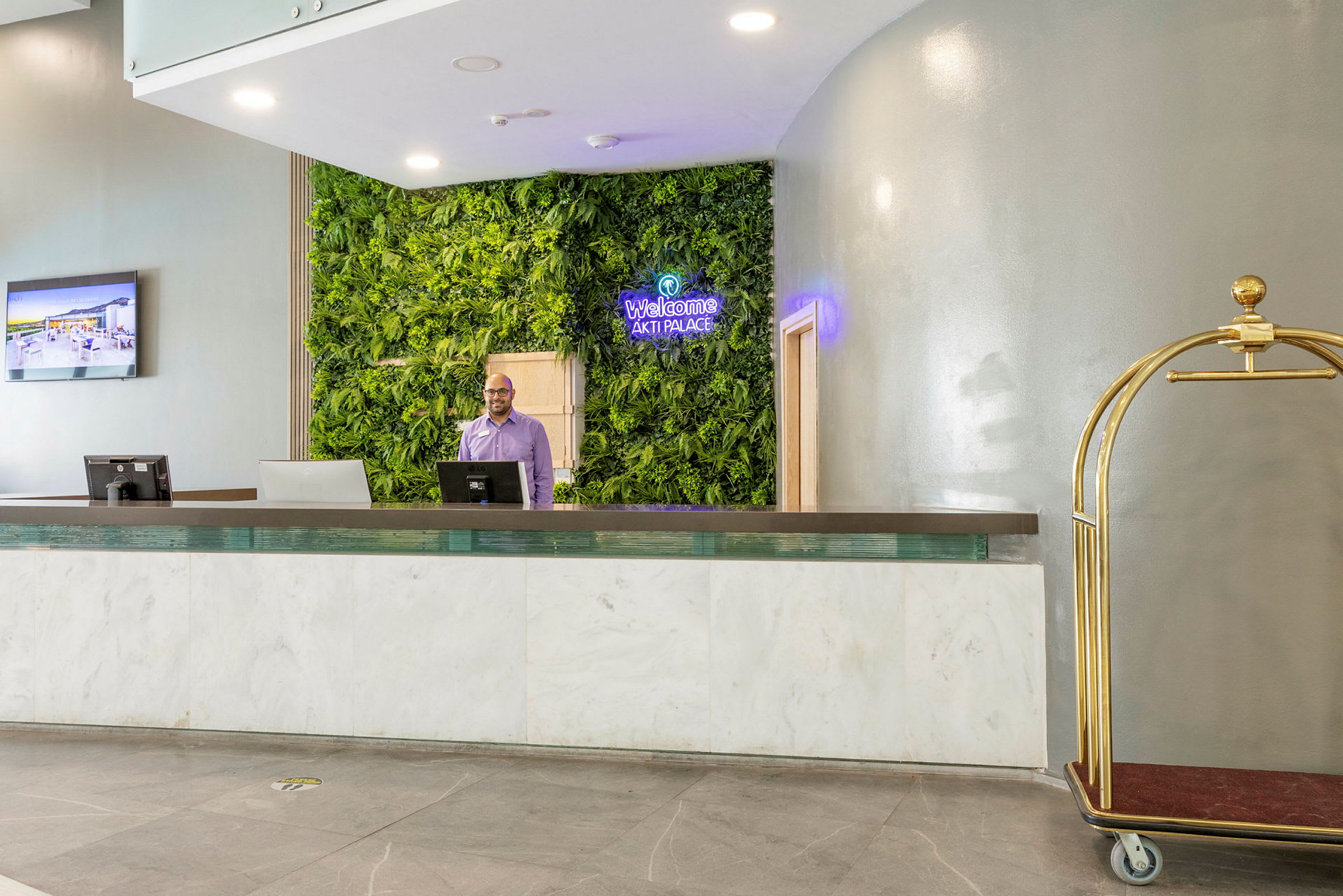 Hotellresepsjon med vegg dekorert med grønne planter og en bagasjevogn. (AI-generert tekst)
