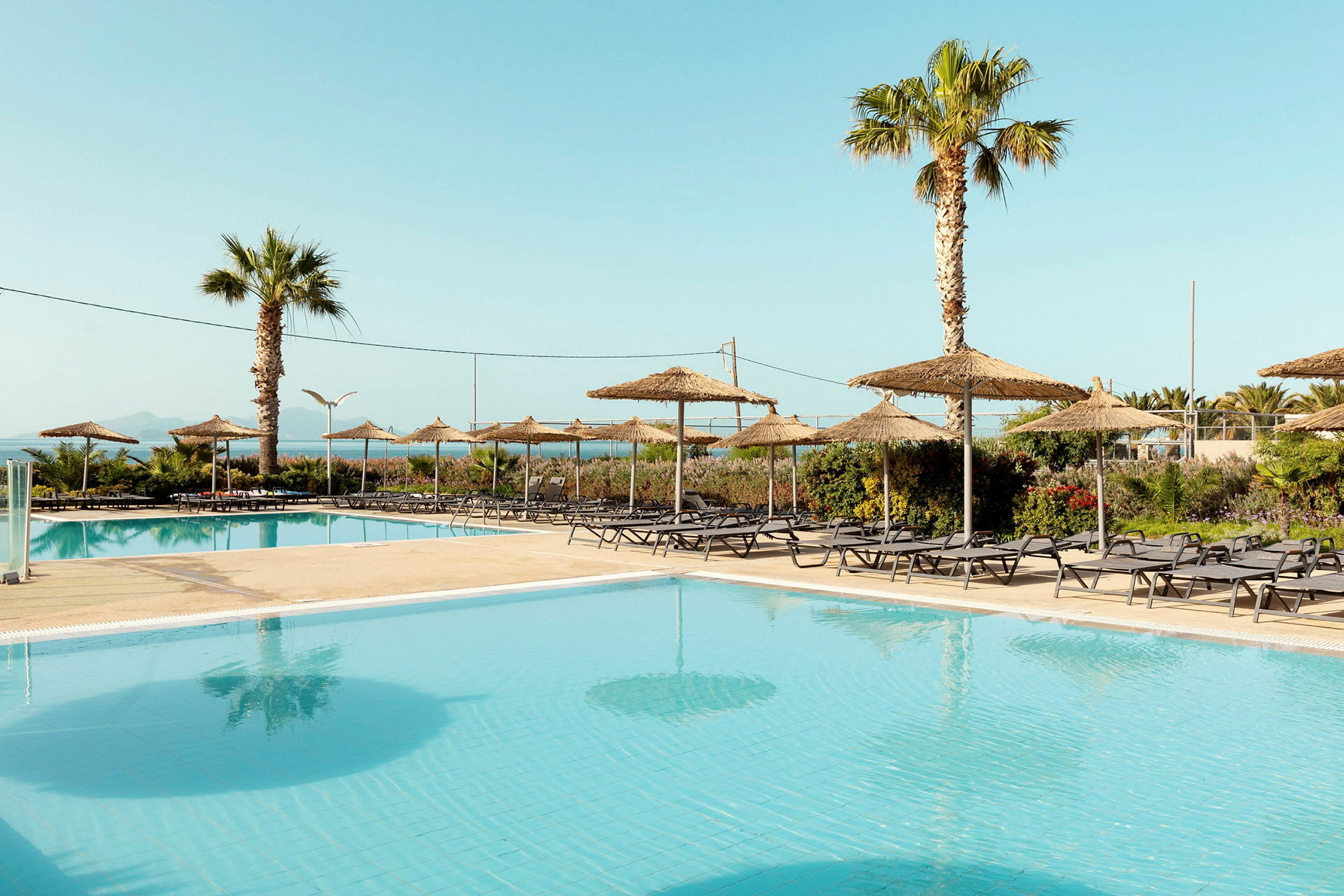 Bilde av et basseng med solsenger og parasoller i en hotellresort-miljø. (AI-generert tekst)