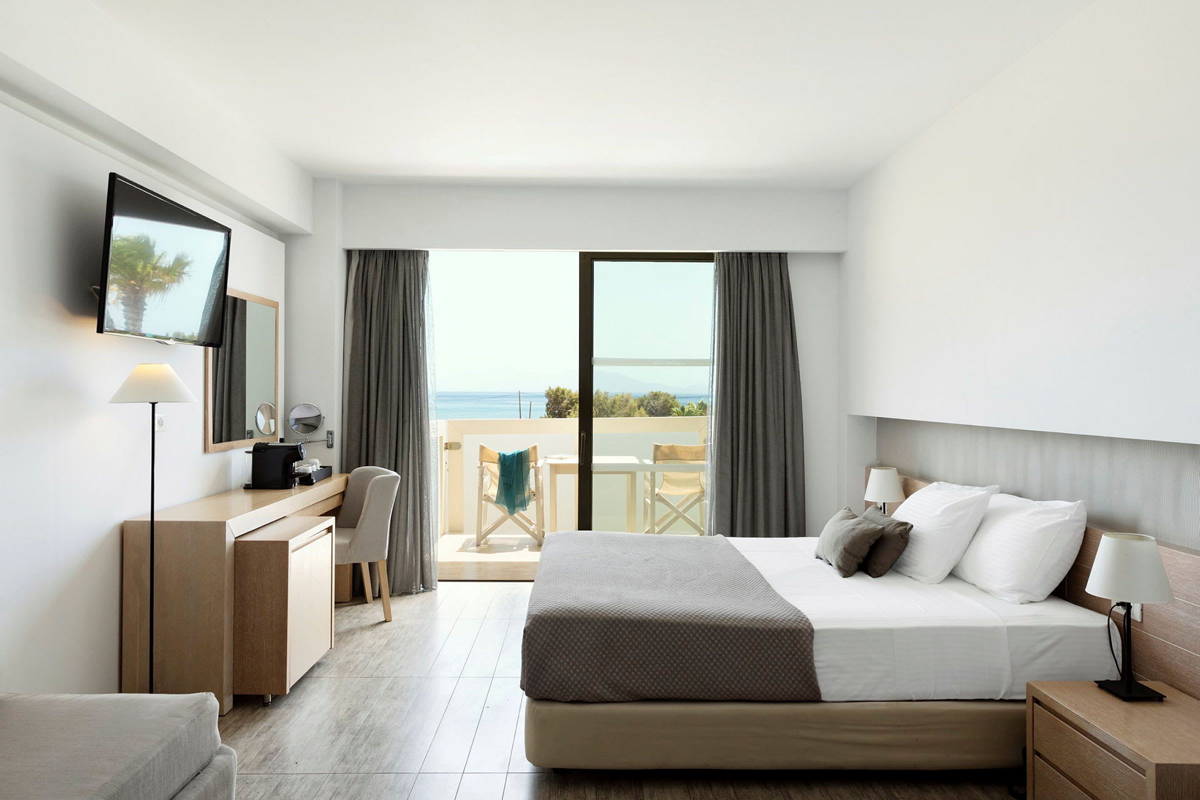 Et hotellrom med en dobbeltseng, skrivebord og en balkong med utsikt over havet. (AI-generert tekst)