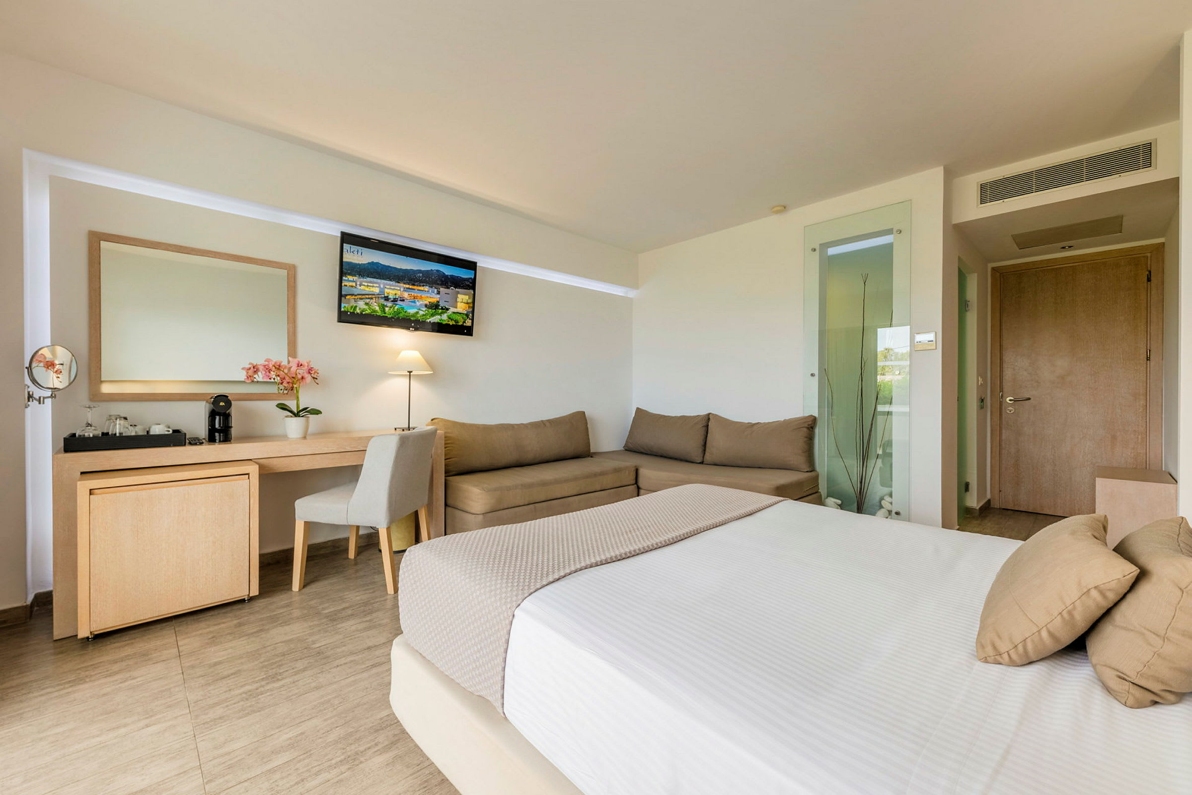 Hotellrom med seng, skrivebord, sofa og TV. (AI-generert tekst)