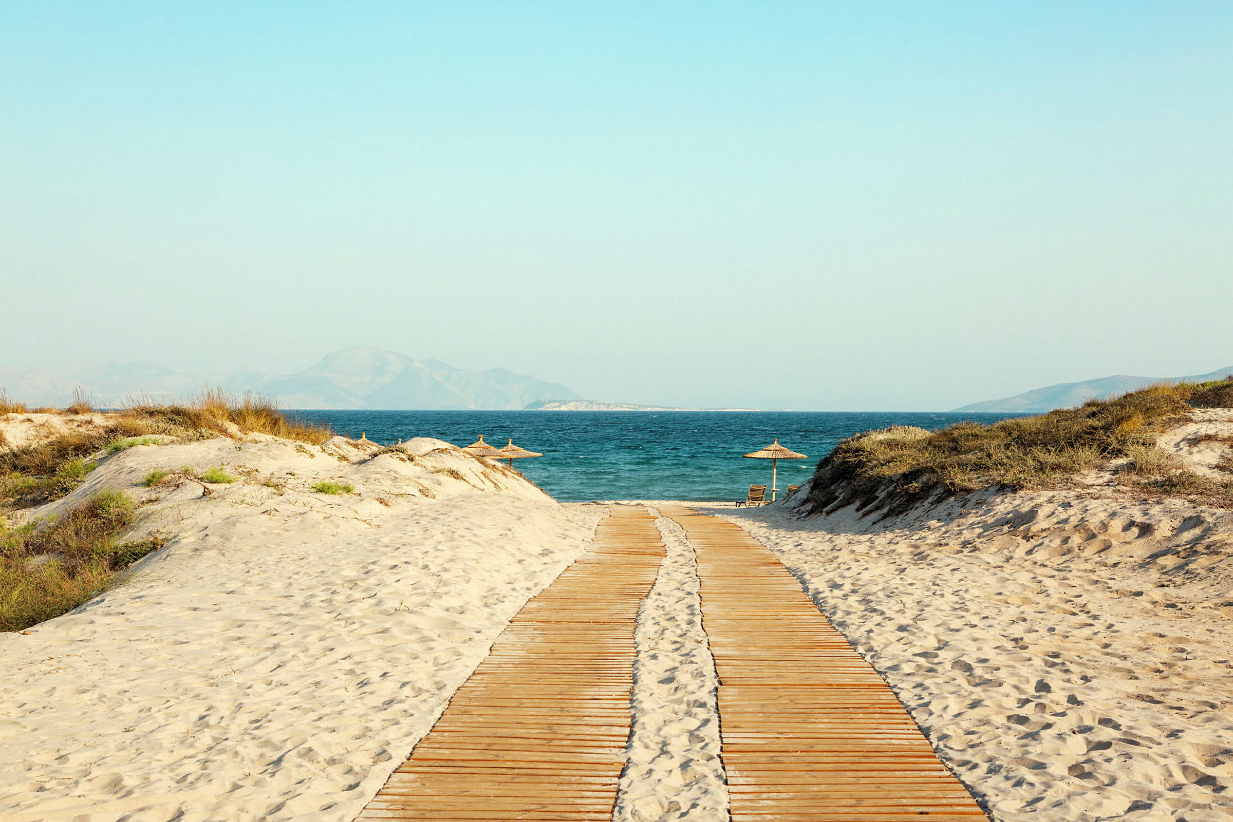 En trebro leder over en sandstrand til havet. (AI-generert tekst)