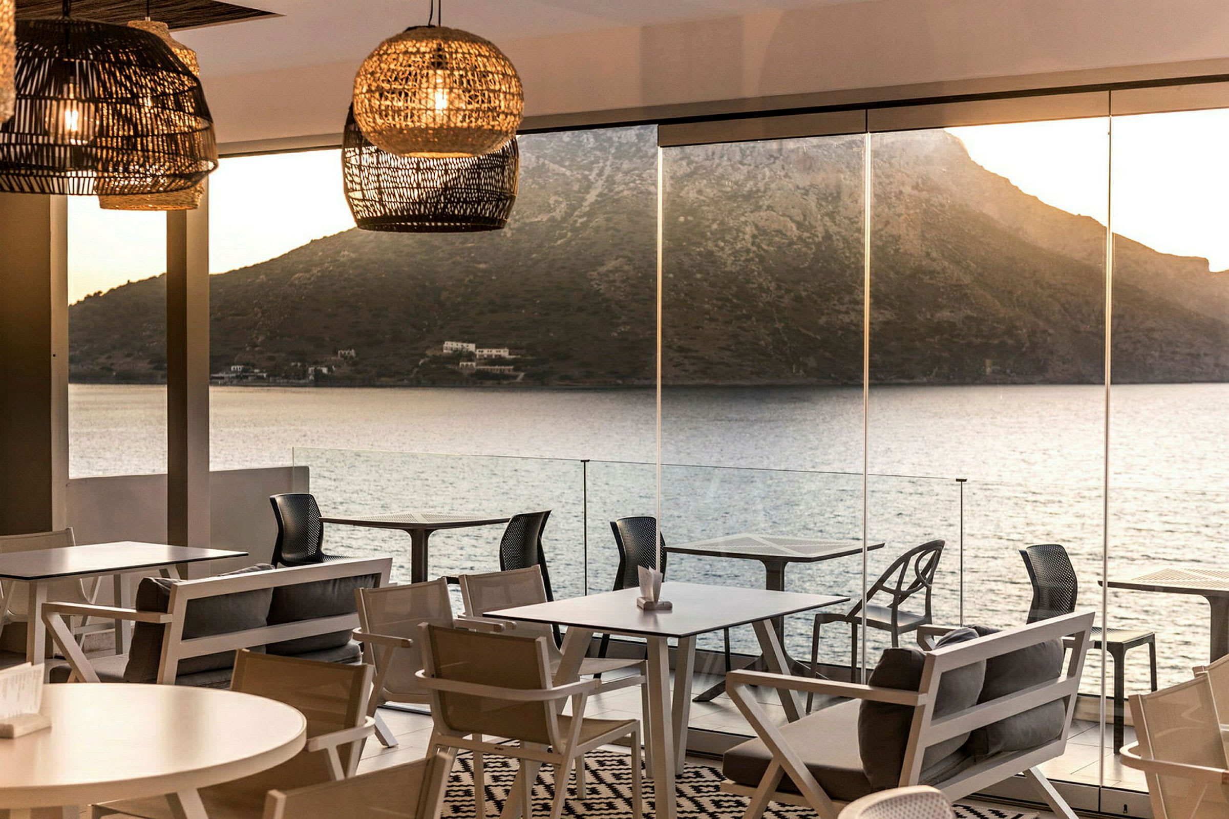 Utsikt over havet og fjellene i bakgrunnen fra en restaurant med store glassvinduer og moderne møbler. (AI-generert tekst)