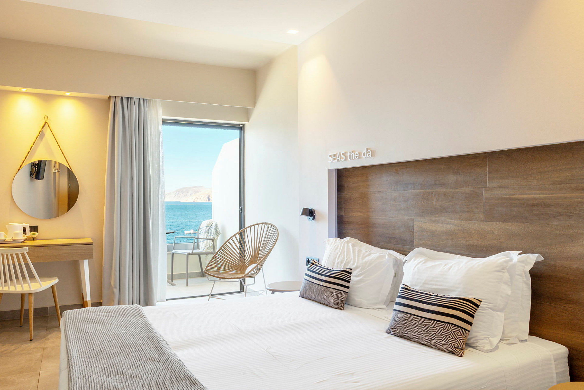 Et hotellrom med moderne interiør, en dobbeltseng, et skrivebord og utsikt over havet fra en balkong. (AI-generert tekst)