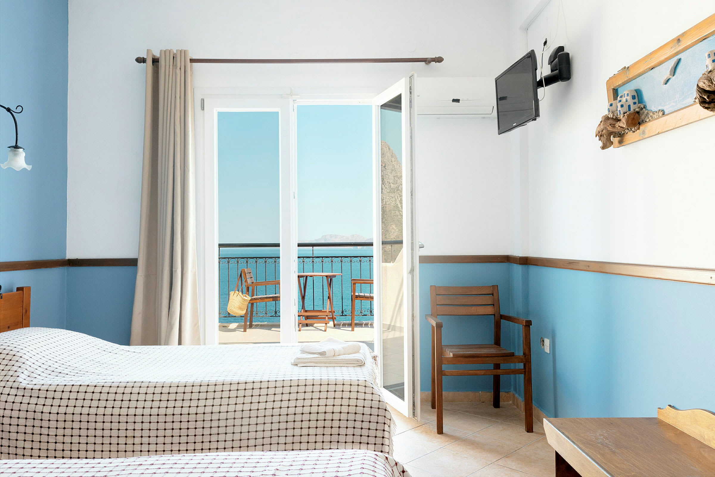 Hotellrom med to senger, utsikt mot en balkong og havet. (AI-generert tekst)