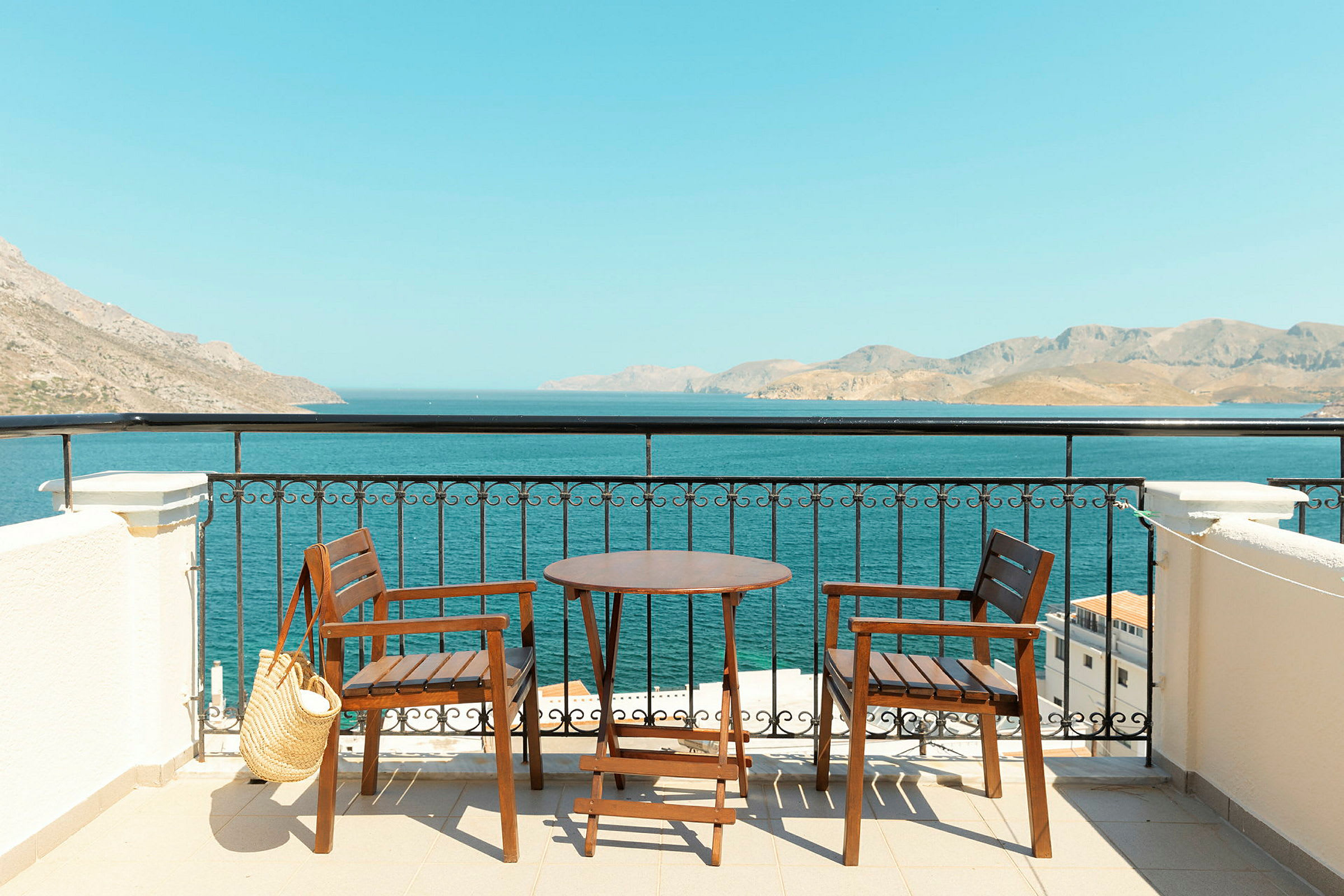 To trestoler og et bord på en terrasse med utsikt over havet og fjell i det fjerne. (AI-generert tekst)