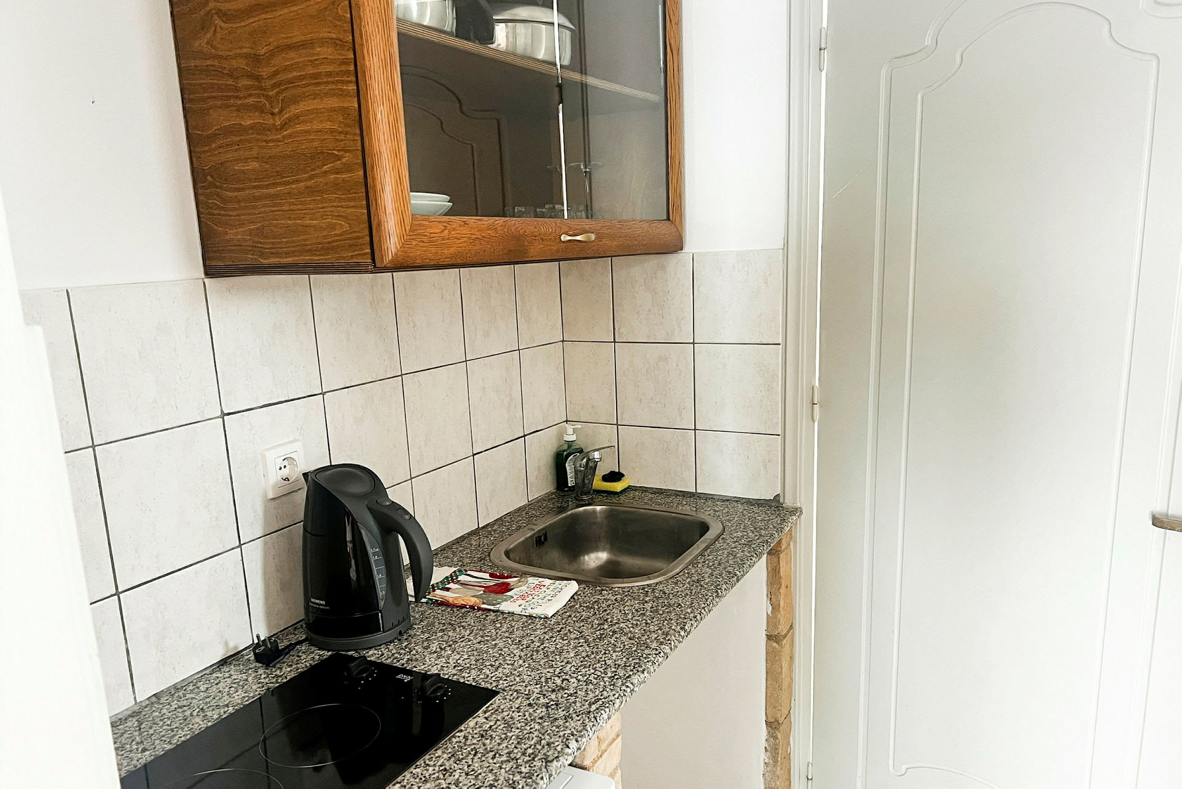 Et lite kjøkken med en vask, en induksjonstopp, en vannkoker og et kabinett. (AI-generert tekst)