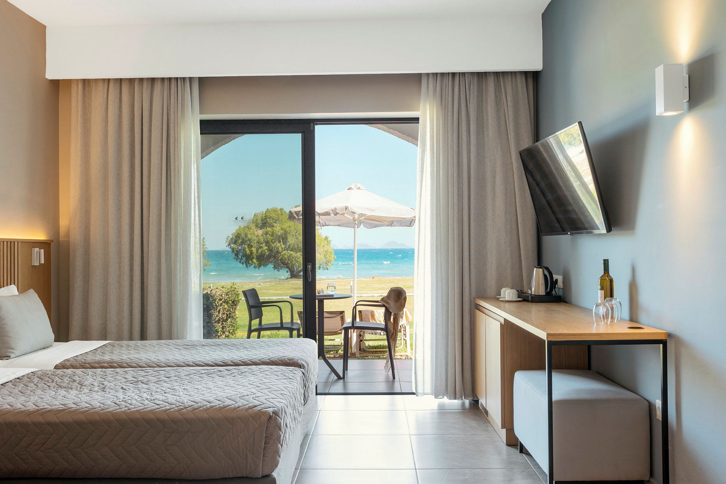 Hotellrom med to enkeltsenger, en åpning mot en møblert terrasse og havutsikt. (AI-generert tekst)