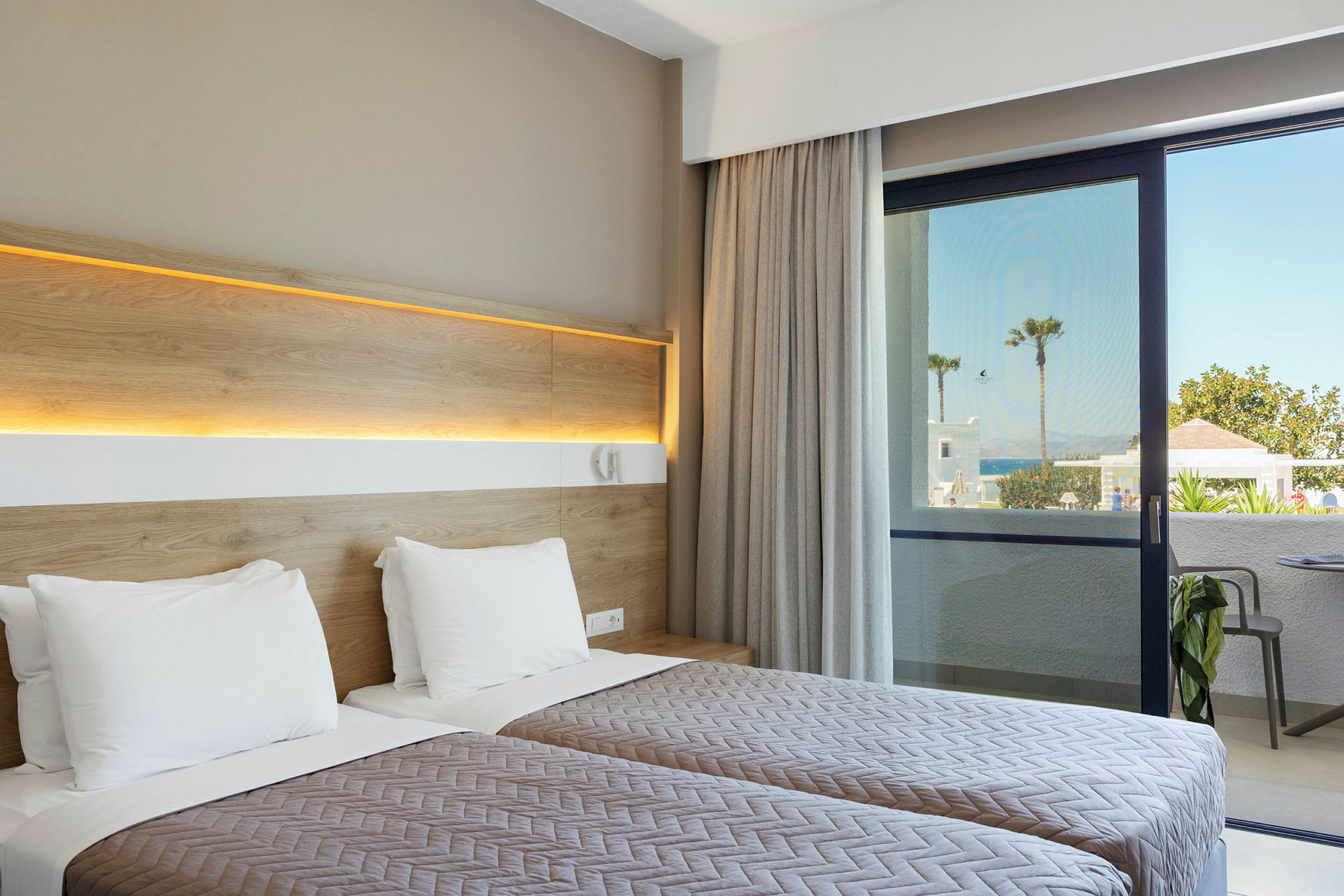 Hotellrom med to enkeltsenger og utsikt mot en uteplass og hav i bakgrunnen. (AI-generert tekst)