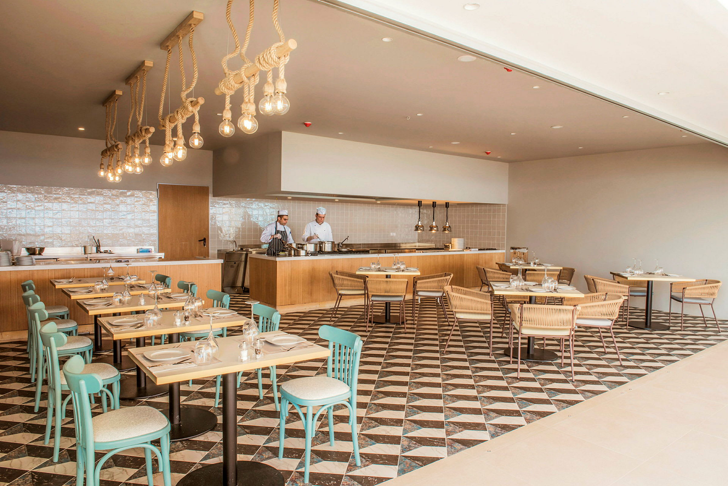 Moderne restaurantinteriør med trebord og turkise stoler, samt et åpent kjøkken med kokker. (AI-generert tekst)