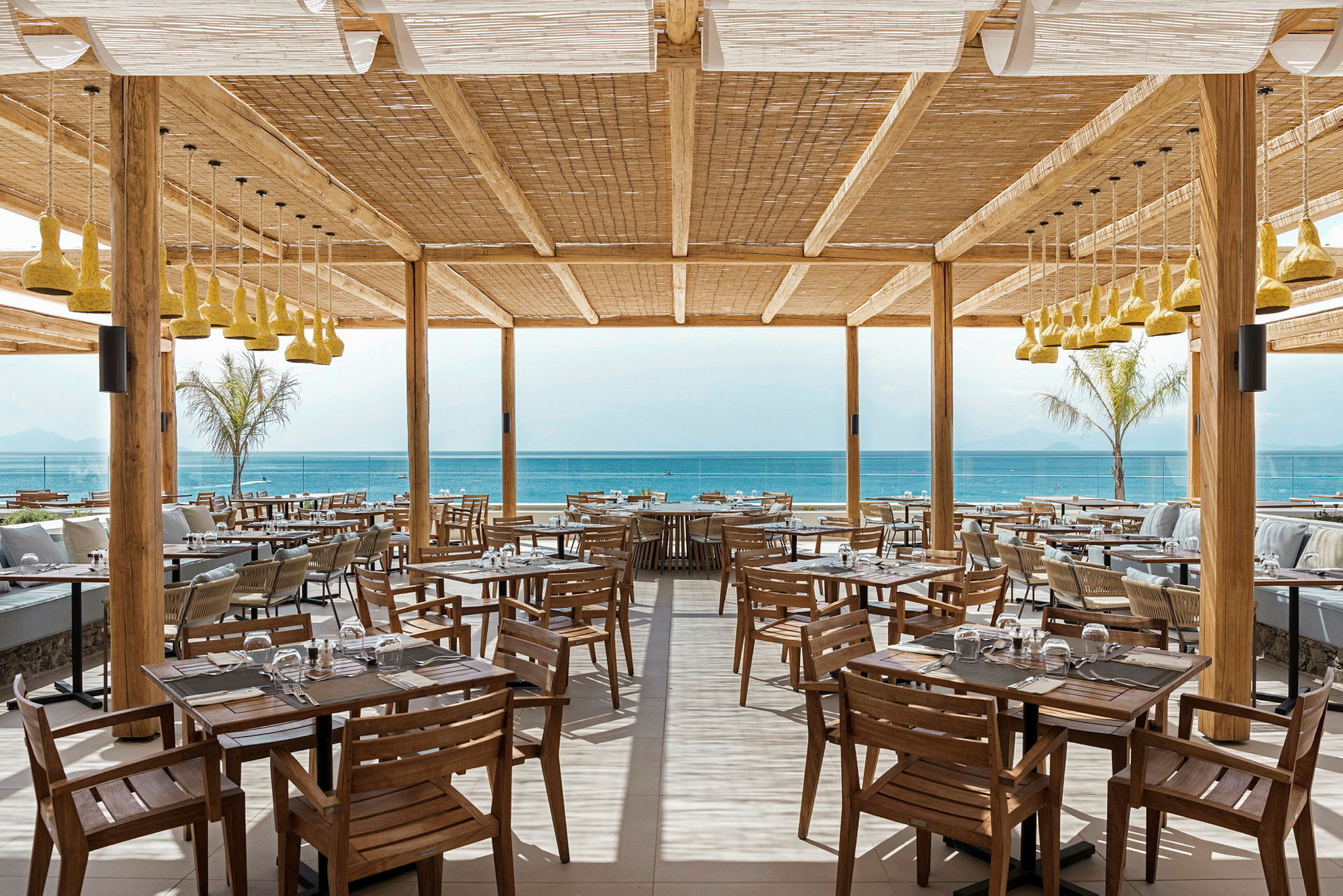 Restaurant med tremøbler og utsikt mot havet. (AI-generert tekst)