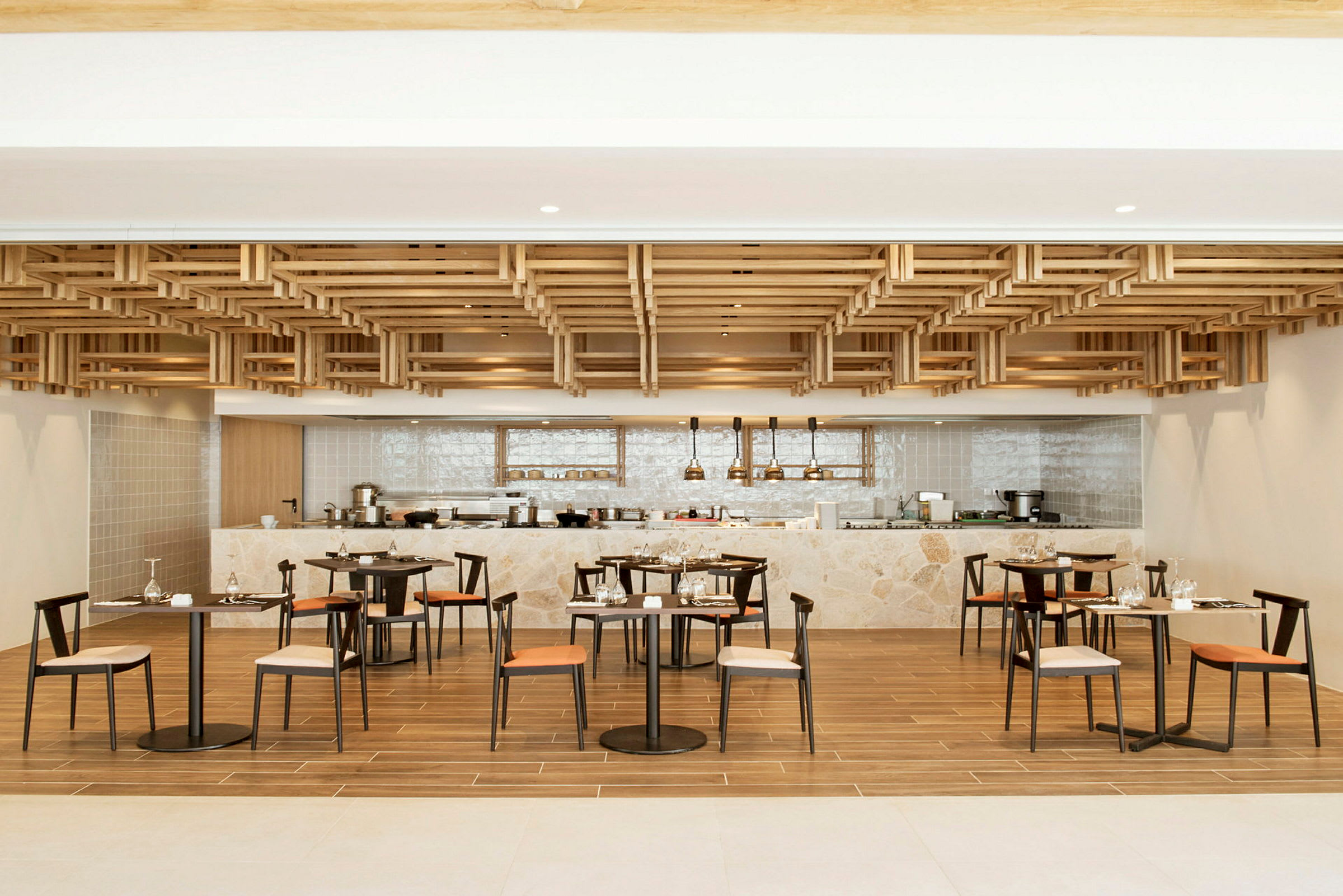 En moderne restaurant med tredetaljer i taket, bord og stoler, og en bardisk i bakgrunnen. (AI-generert tekst)