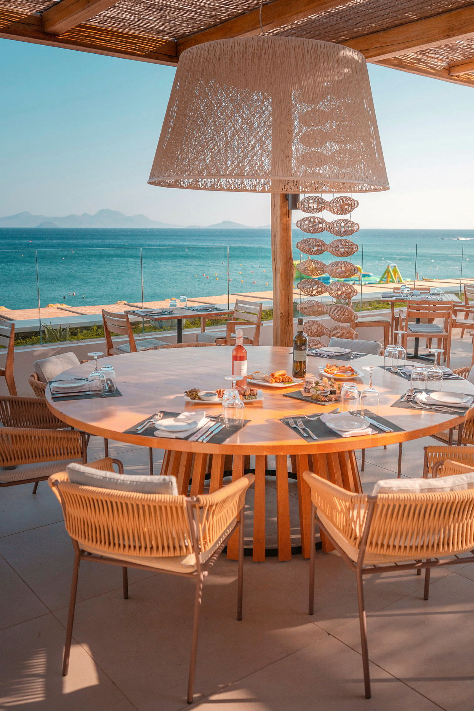 Et dekket trebord med stoler på en restaurantterrasse som vender mot havet. (AI-generert tekst)