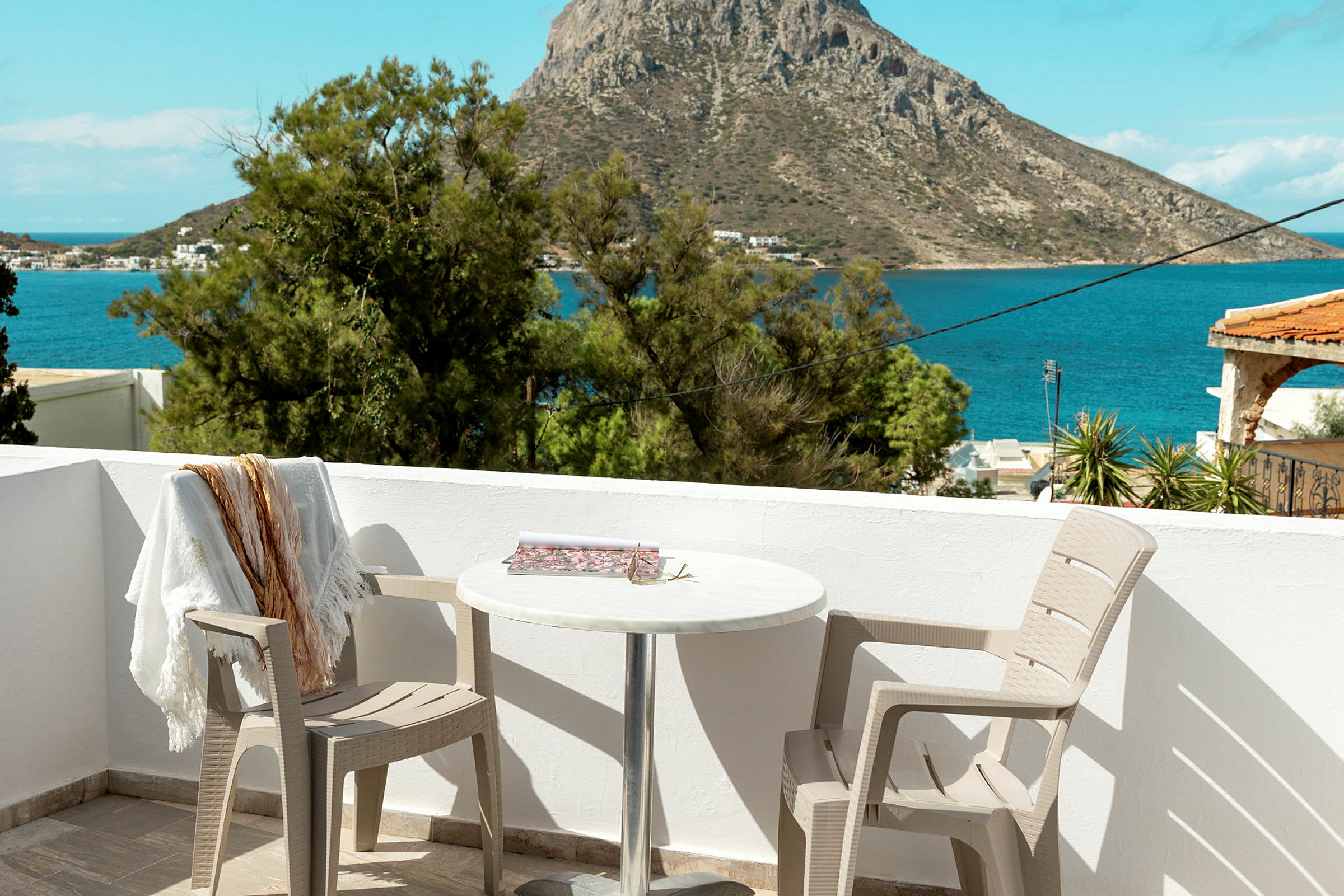 Utsikt fra en terrasse med to stoler og et bord, mot havet og en klippe i bakgrunnen. (AI-generert tekst)